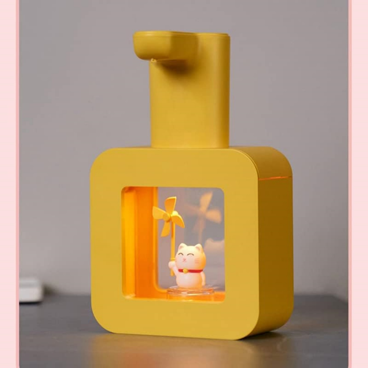 Gelber Dispenser mit Lucky Cat Figur und Windrad im Fenster.