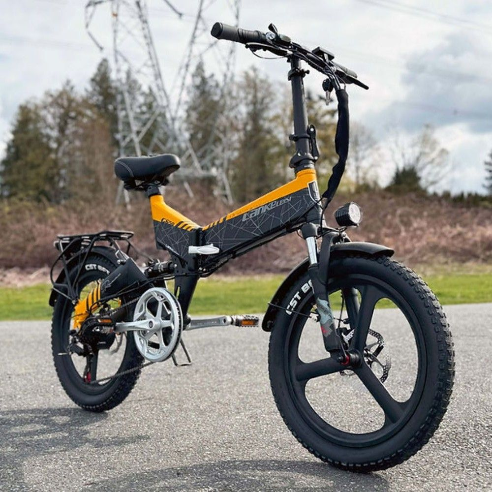 Una bicicleta eléctrica amarilla y negra aparcada en asfalto con cables y árboles detrás.