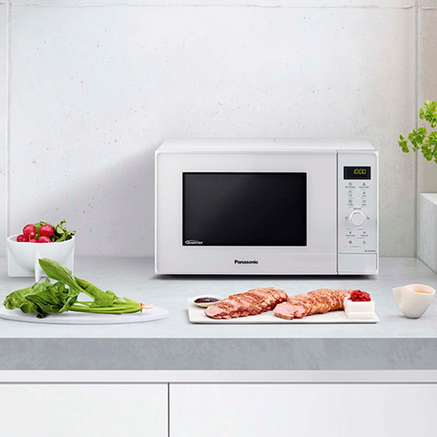 White microwave with sliced meat, greens, and radishes on a kitchen counter.