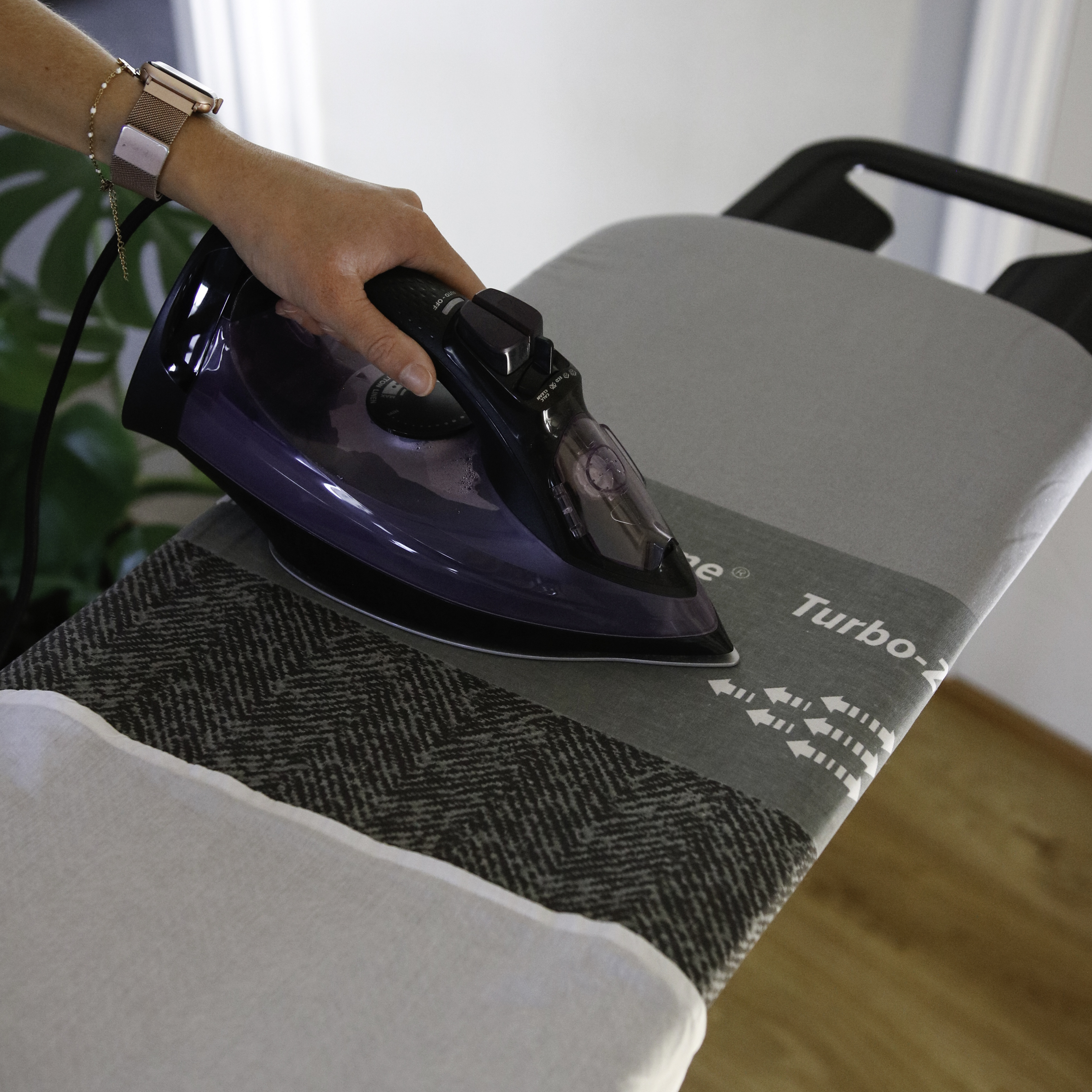Eine Hand bügelt mit einem lila Bügeleisen auf einem Bügelbrett.
