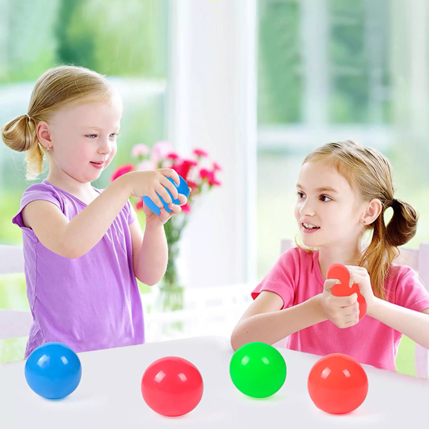 Dos niñas juegan con pelotas de colores frente a una ventana.