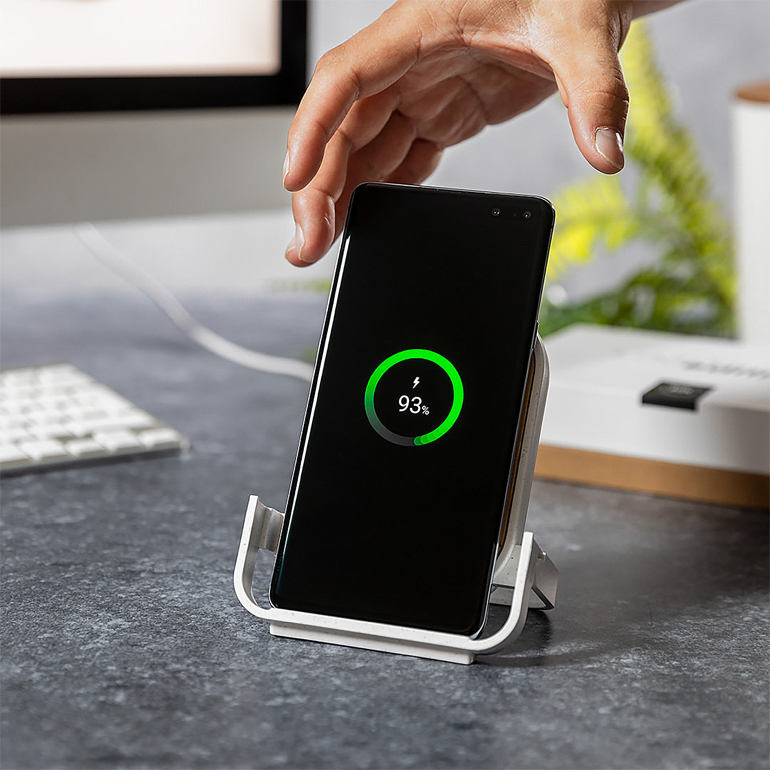 Una mano posiziona un telefono su un caricabatterie. 93% carico.
