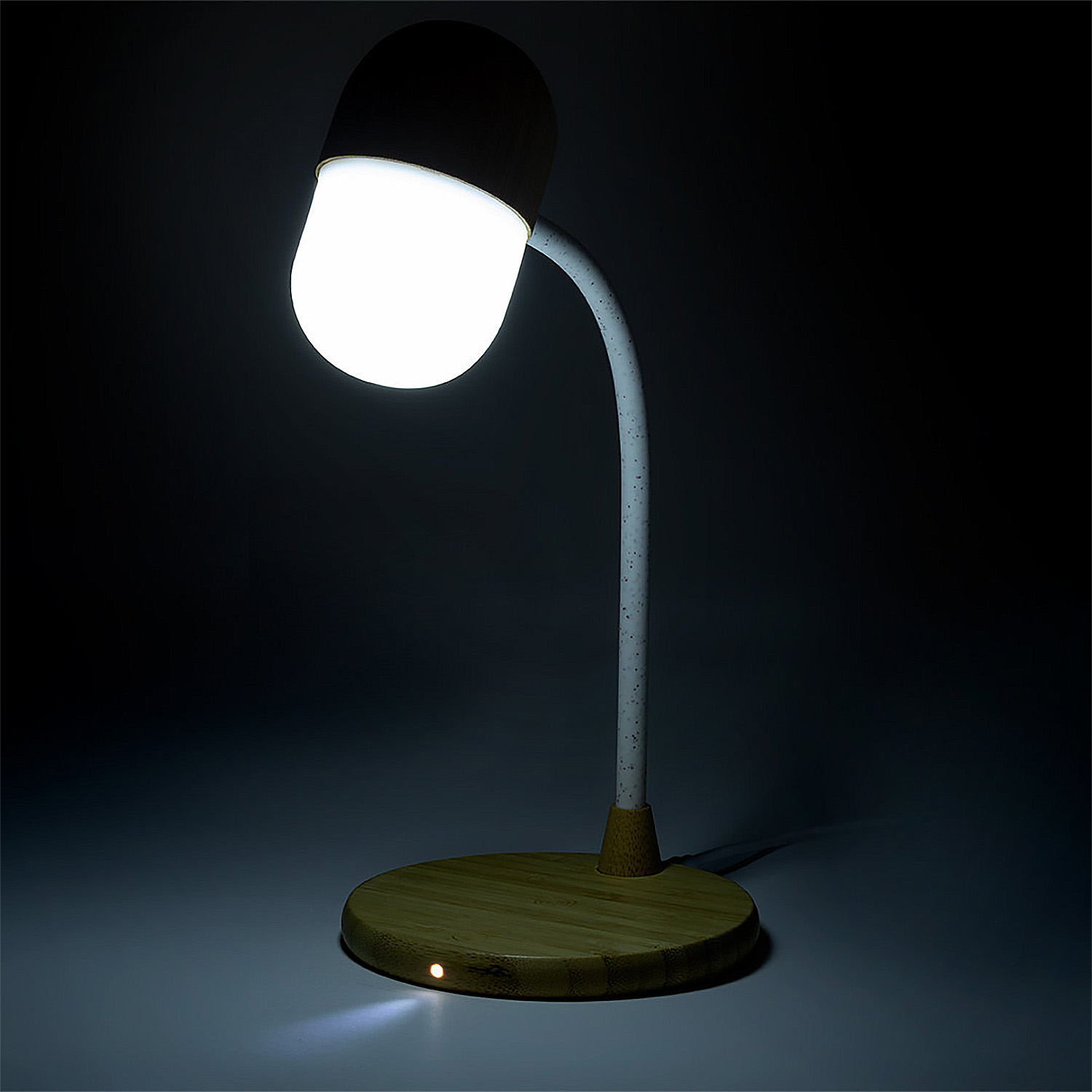 Una lampada moderna con base in legno, braccio curvo e paralume bianco illuminato, su sfondo scuro.
