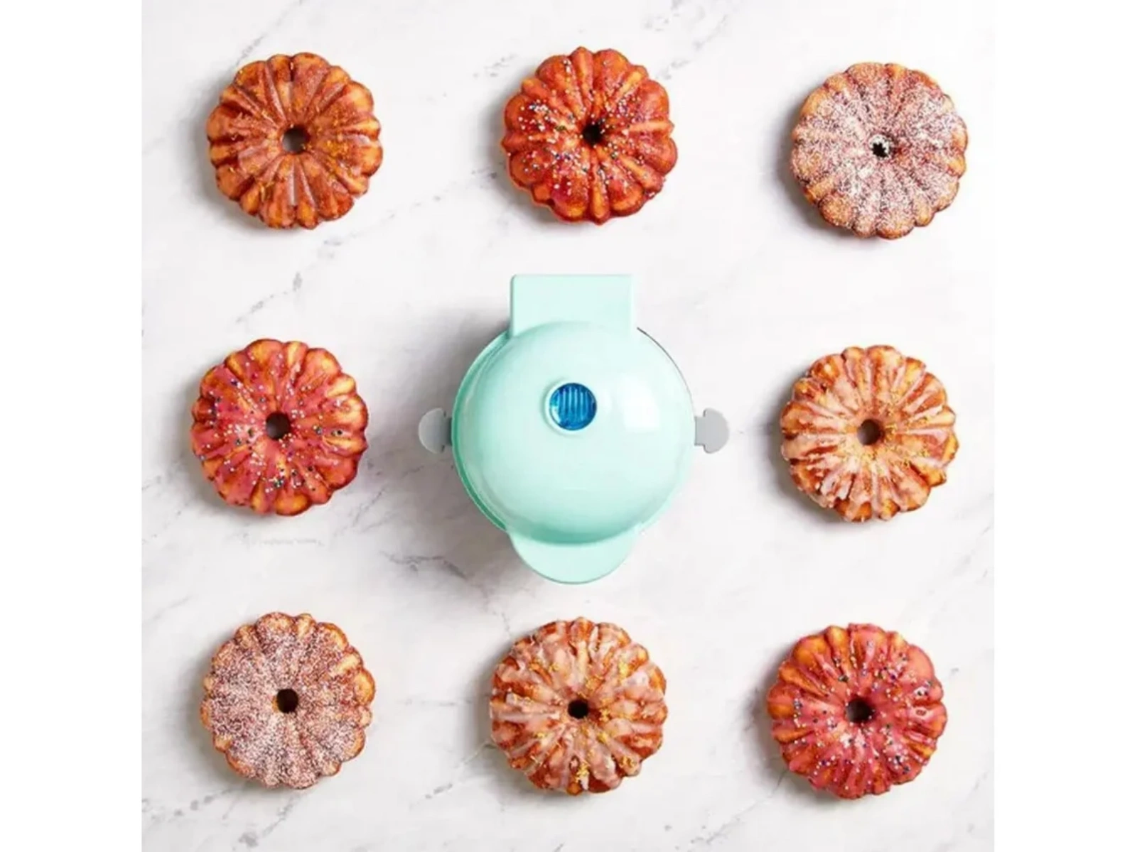 Ein türkisfarbener Mini-Waffelautomat mit acht gebackenen Kuchen drumherum.
