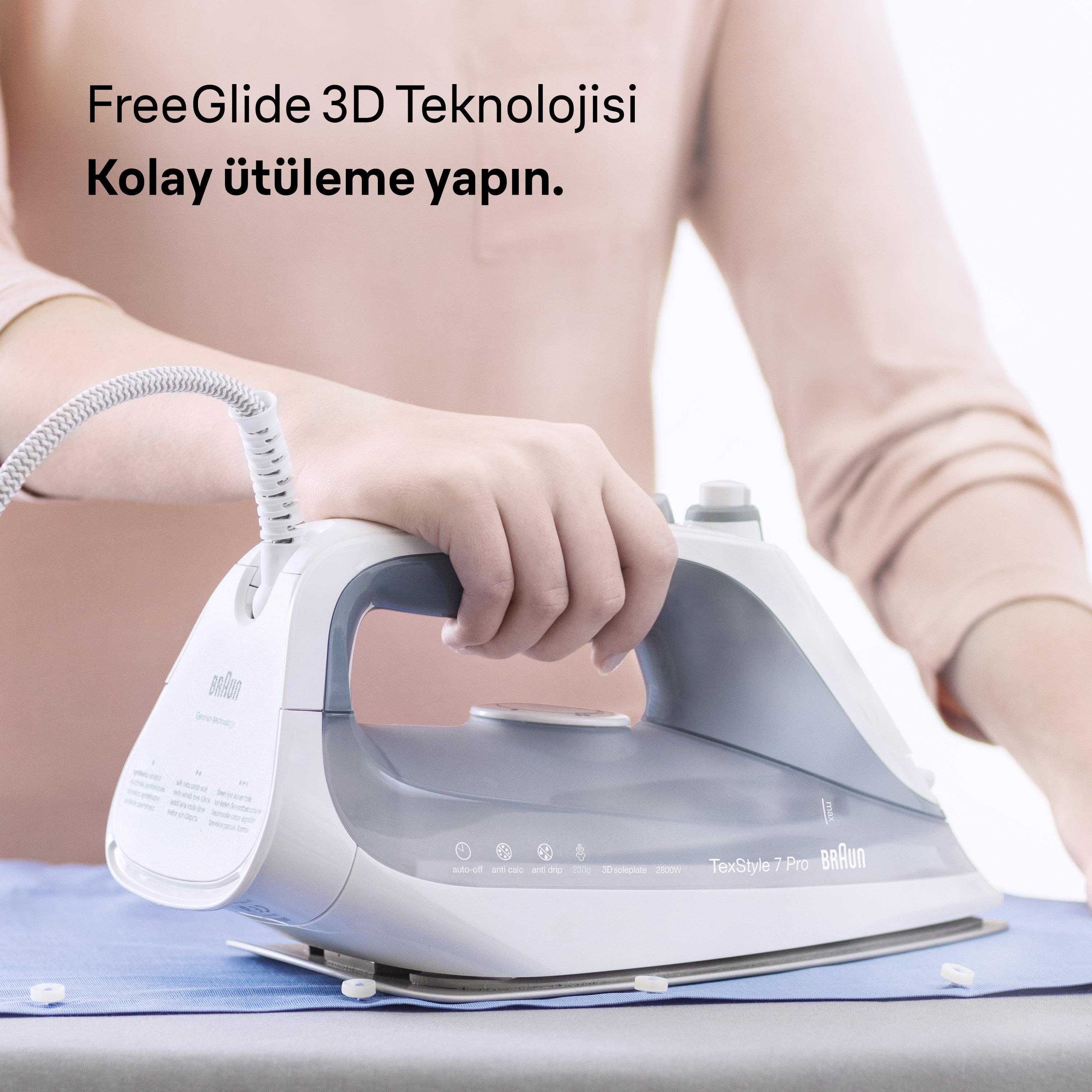 Gri vurgulara sahip beyaz bir Braun ütü, mavi bir gömleğin üzerinde duruyor.