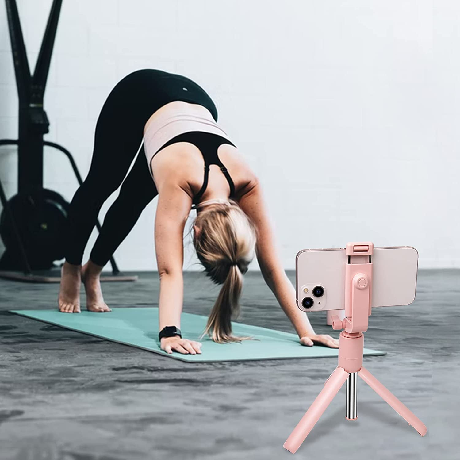 Frau in Downward Dog auf Matte, Handy-Stativ im Vordergrund.