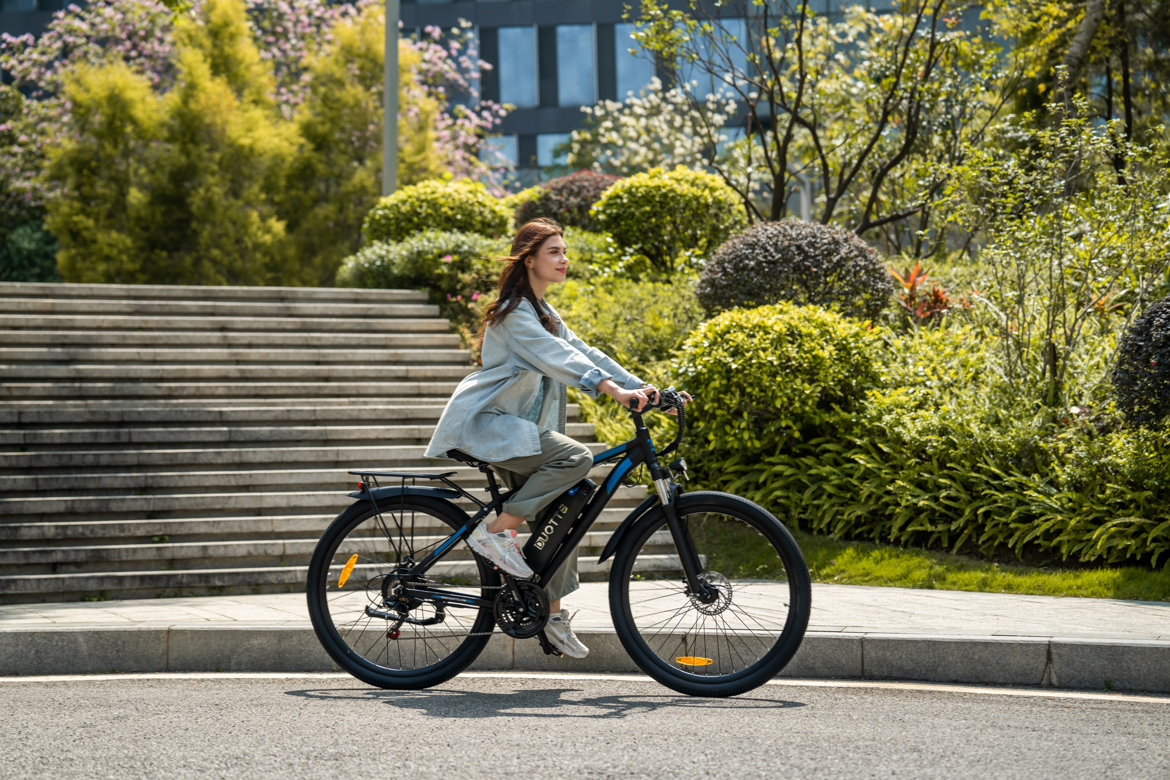 Frau fährt Fahrrad auf Straße vor Treppen und Büschen.