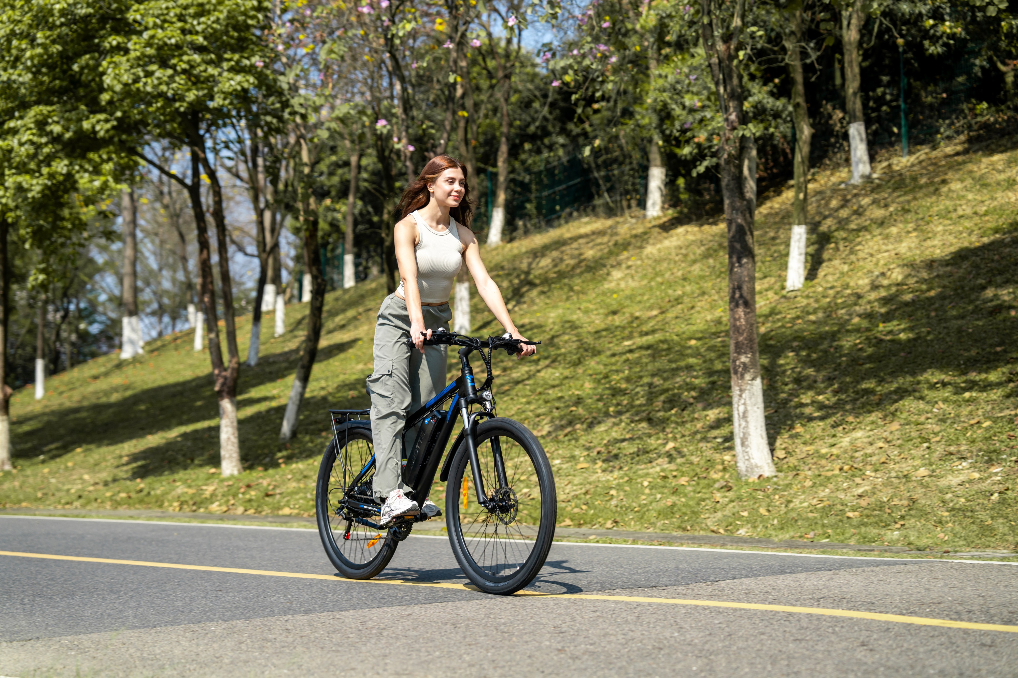 Eine Frau fährt ein schwarzes E-Bike auf einer Straße mit Bäumen und Gras.