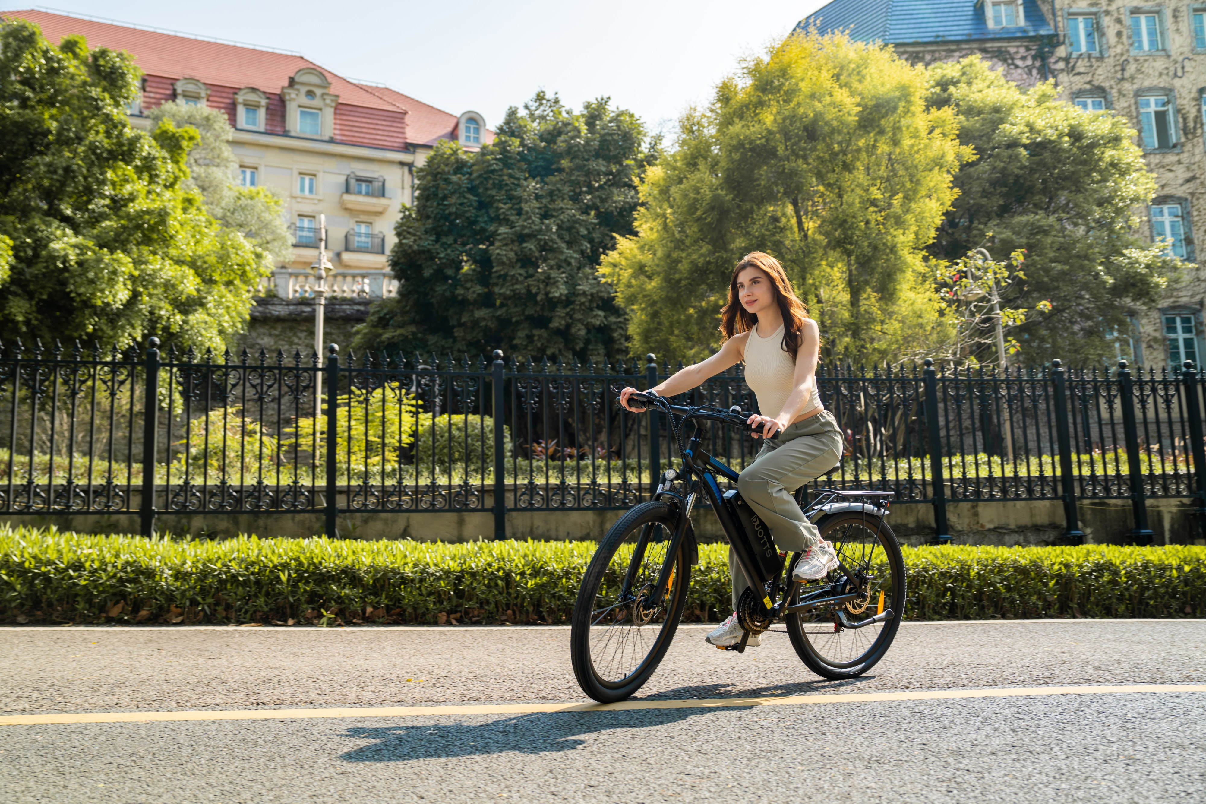 Eine Frau fährt ein schwarzes E-Bike auf einer Straße vor einem alten Gebäude.