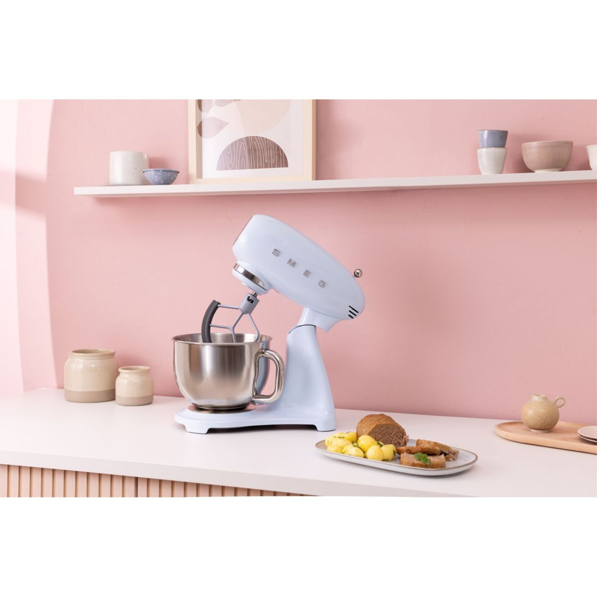 Un robot da cucina Smeg azzurro con ciotola in acciaio inox su un piano di lavoro bianco.