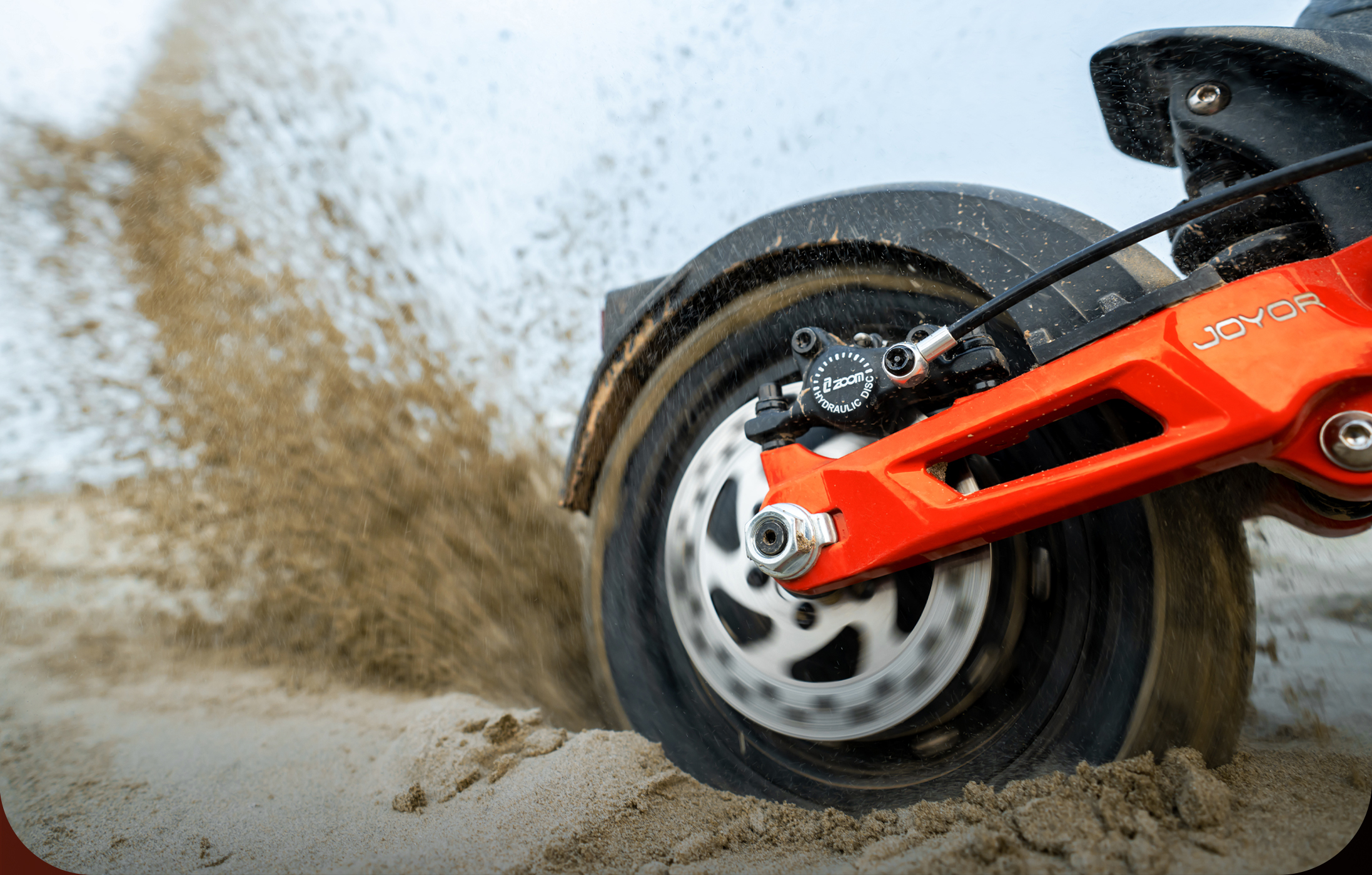Ein E-Scooter-Rad fährt durch Sand und wirbelt ihn auf.