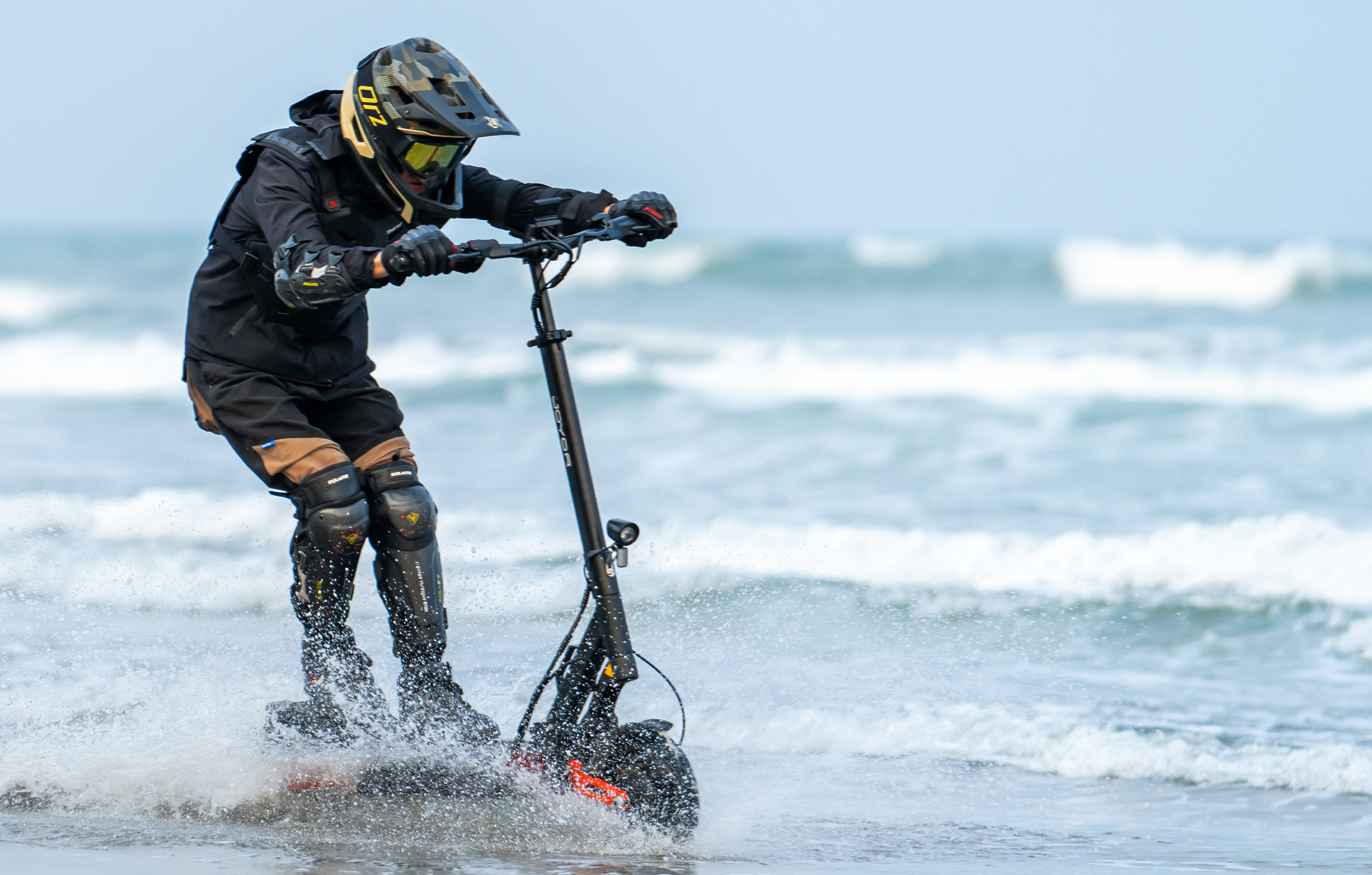 Fahrer auf E-Scooter fährt durch Wellen am Strand.