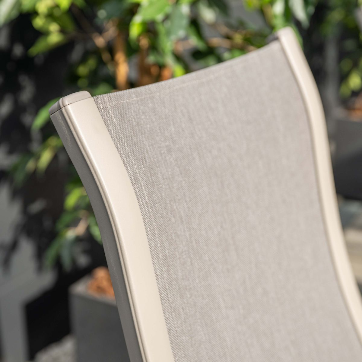 Grijze stoffen stoel met beige rand buitenshuis, met planten op achtergrond.