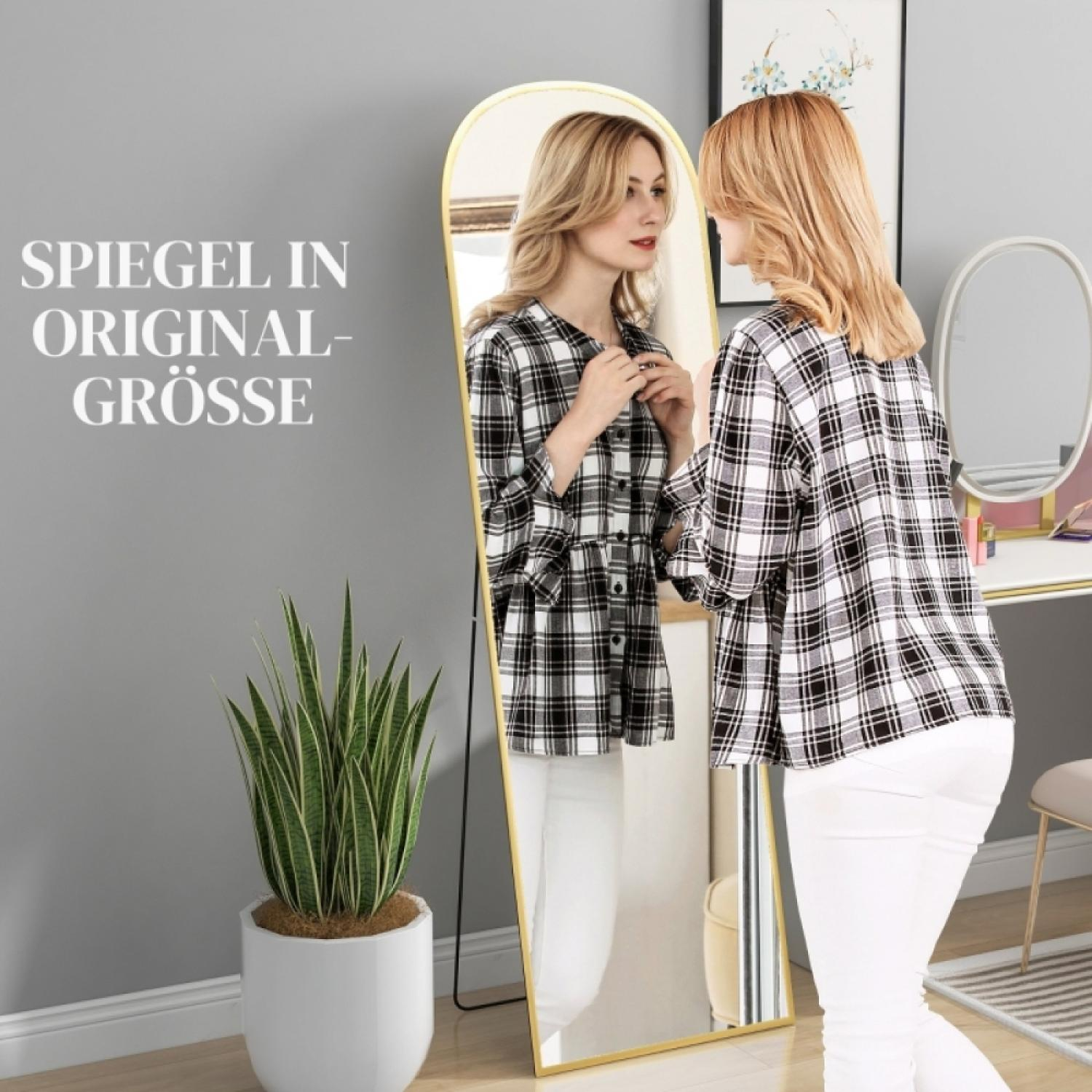 Eine Frau mit blonden Haaren steht vor einem großen Spiegel und betrachtet sich.
