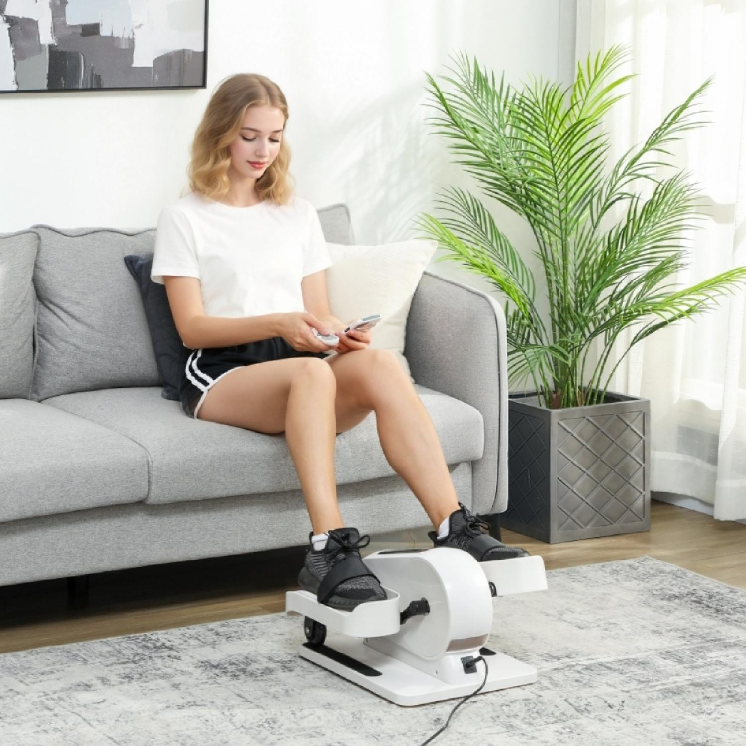 Eine Frau sitzt auf einem Sofa und benutzt einen kleinen Heimtrainer für die Füße.
