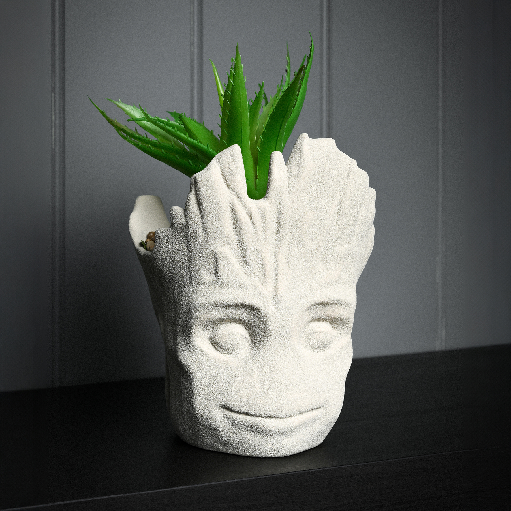 Ein weißer Blumentopf in Form von Groots Kopf mit einer grünen Pflanze.