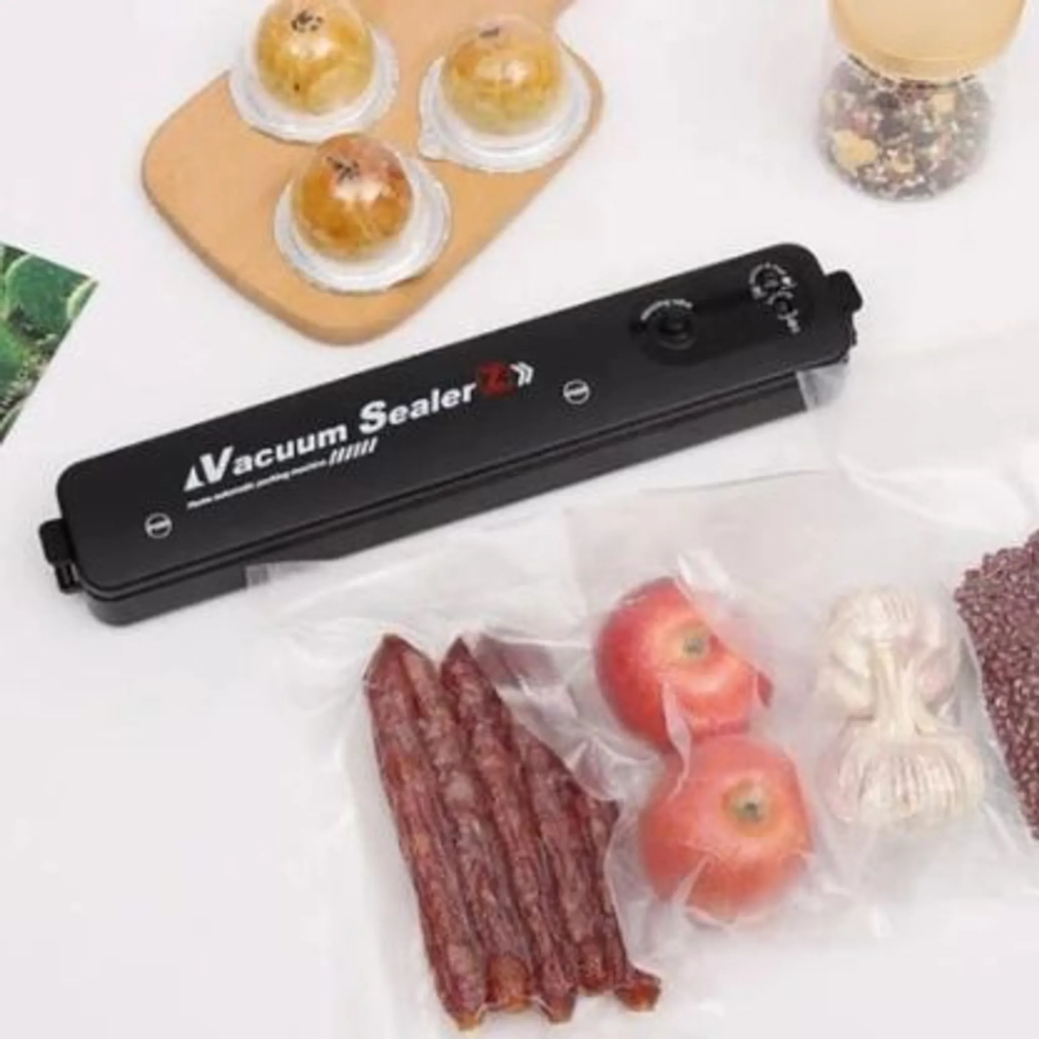 Ein schwarzes Vakuumiergerät mit Wurst, Äpfeln, Knoblauch und Gebäck.