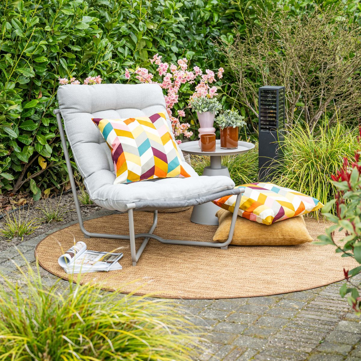 Grijze loungestoel met kussens op een ronde jutte mat in de tuin.