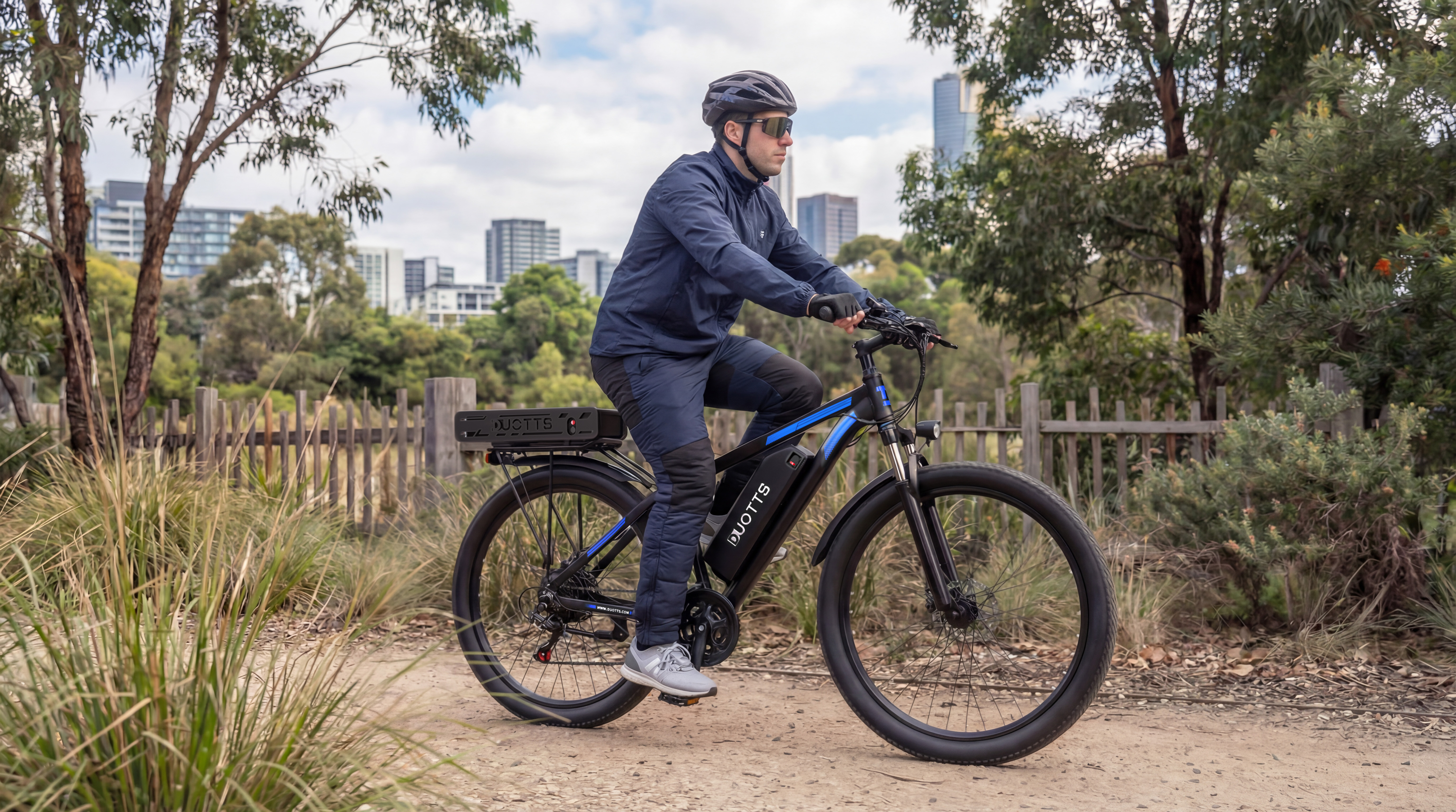 Mann fährt E-Bike auf Schotterweg mit Stadtblick im Hintergrund.
