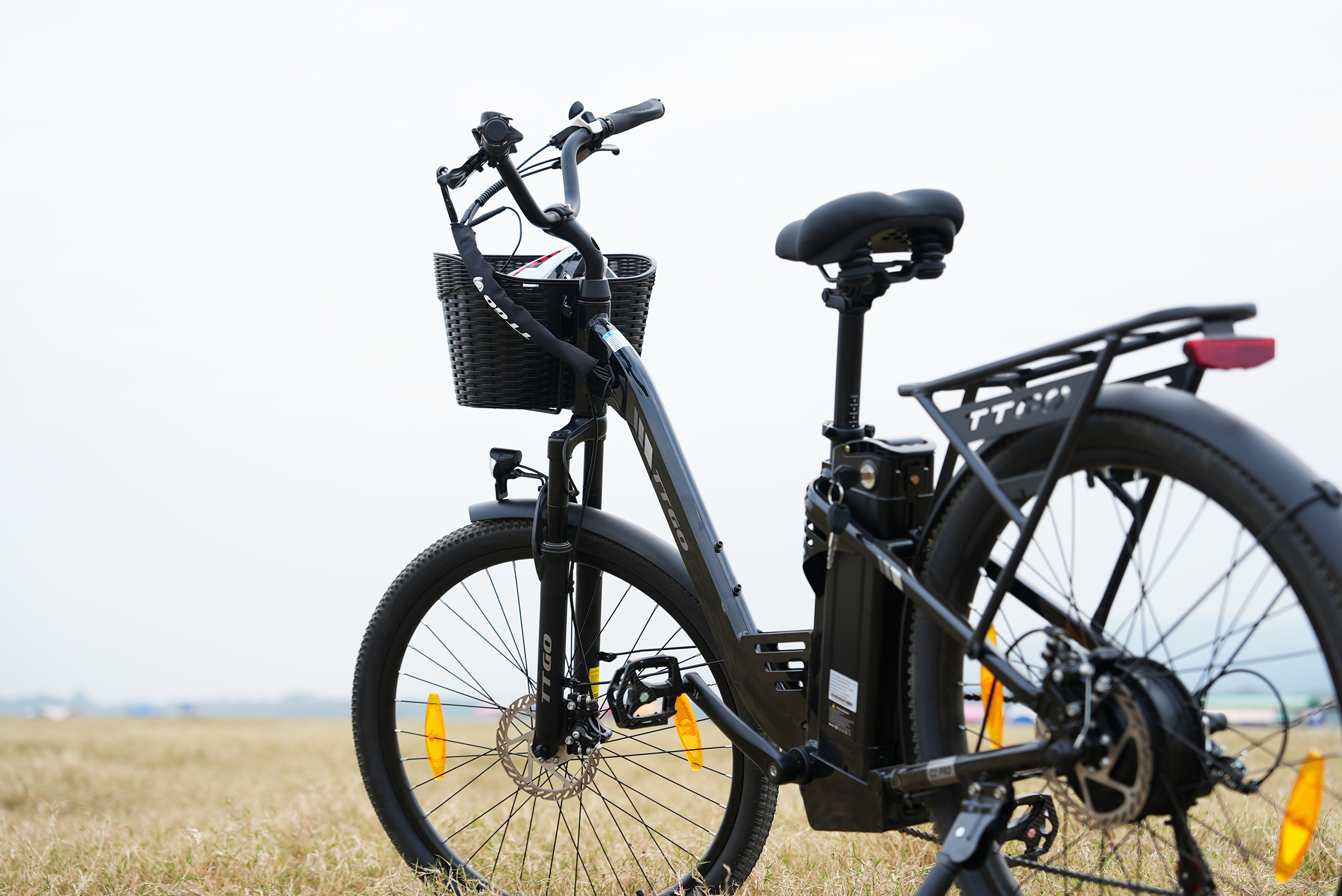 Ein schwarzes E-Bike mit Korb und Akku steht auf trockenem Gras.