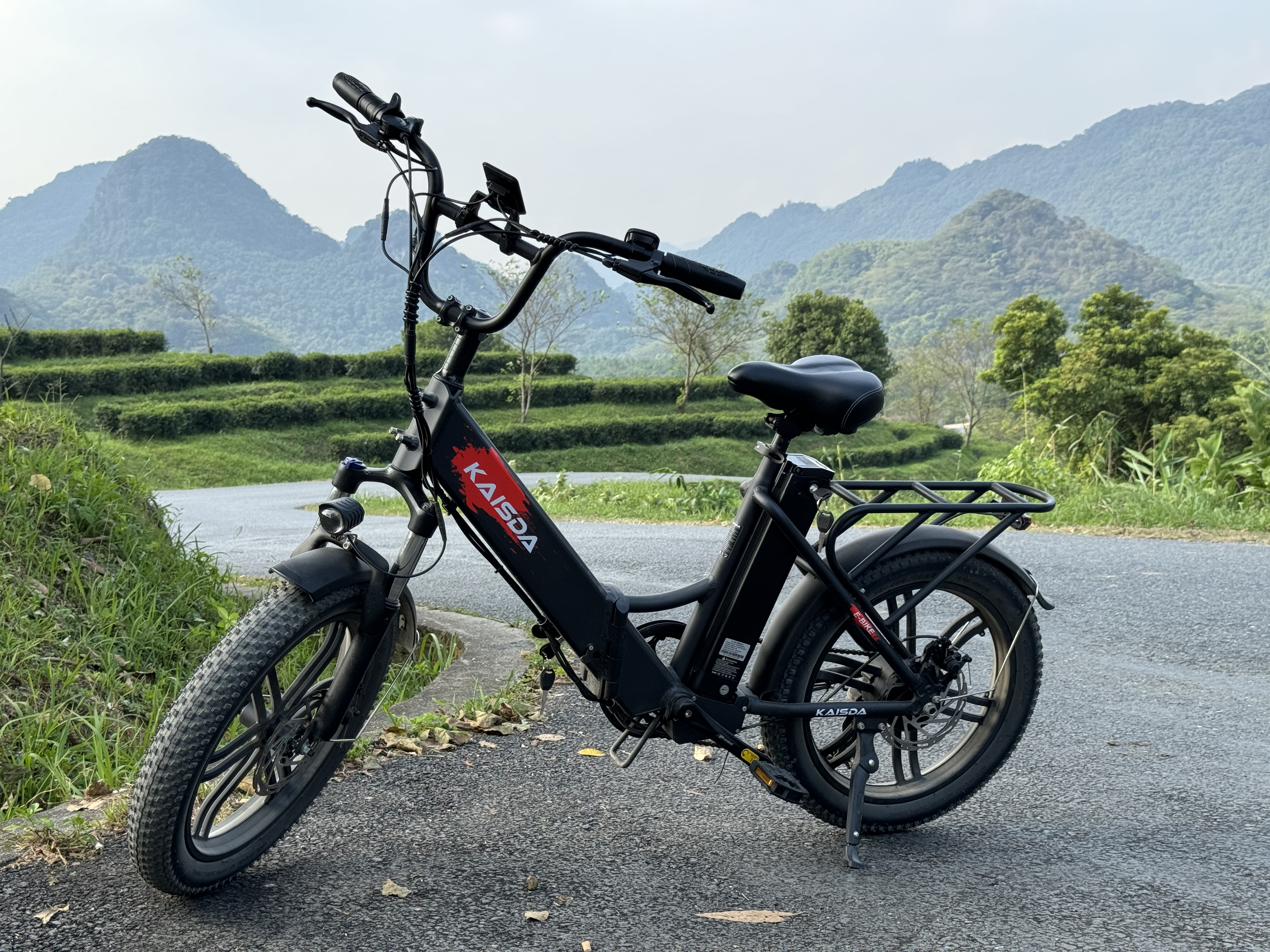 Ein schwarzes E-Bike steht auf einer asphaltierten Straße mit Bergen und Teefeldern im Hintergrund.
