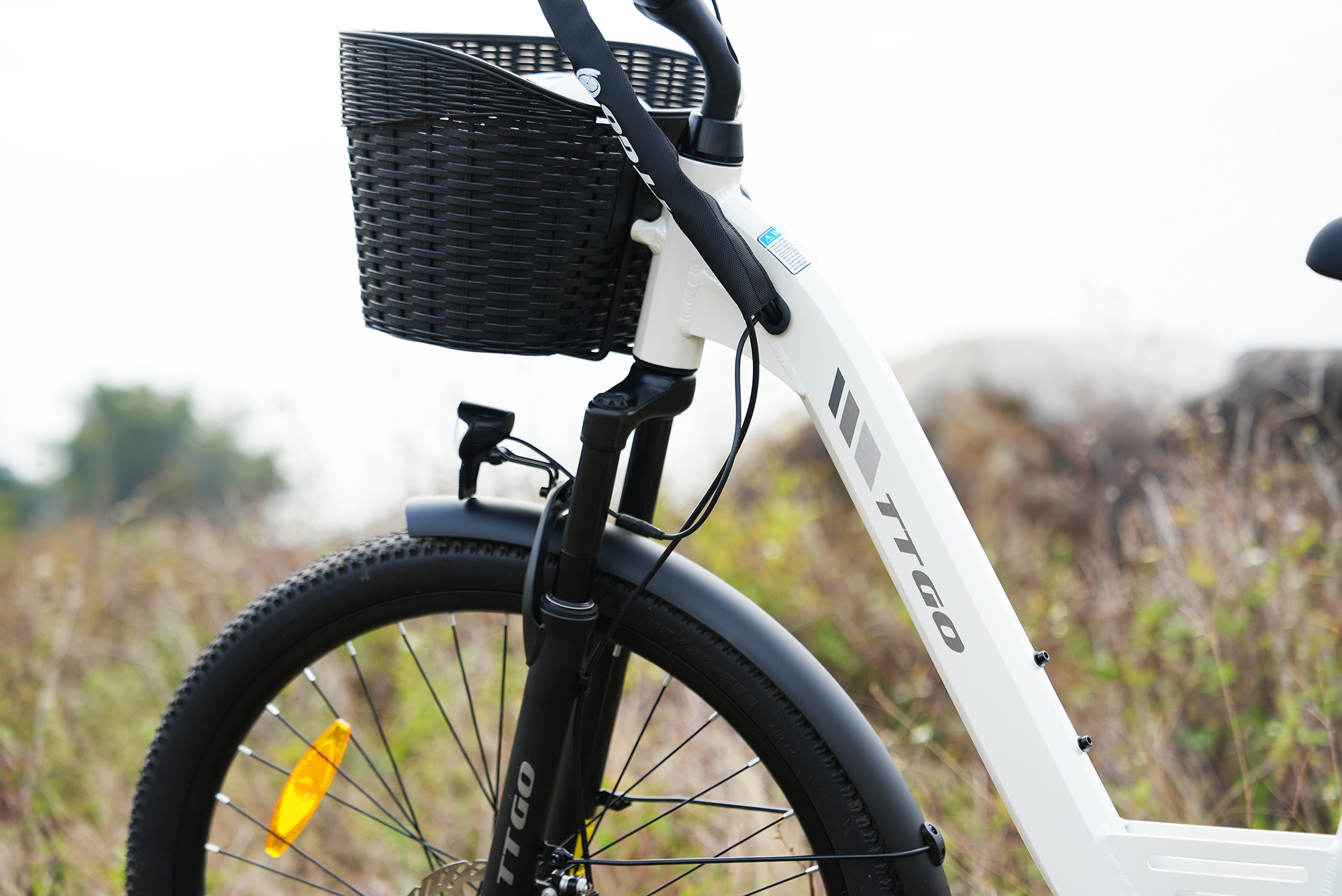 Ein weißes E-Bike mit schwarzem Korb und Vorderrad ist im Freien abgebildet.