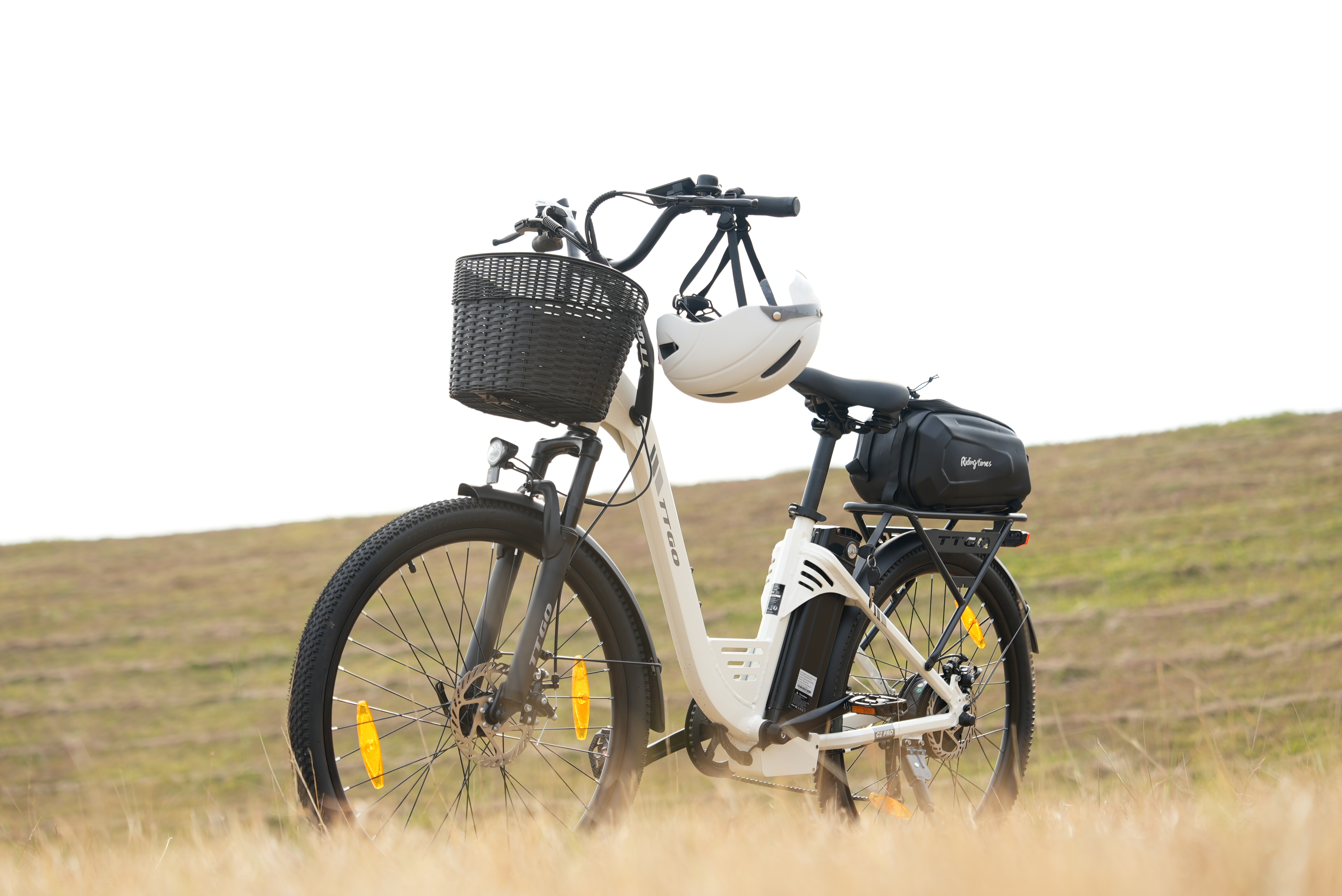 Ein weißes E-Bike mit Korb, Helm und Gepäcktasche steht im Gras.