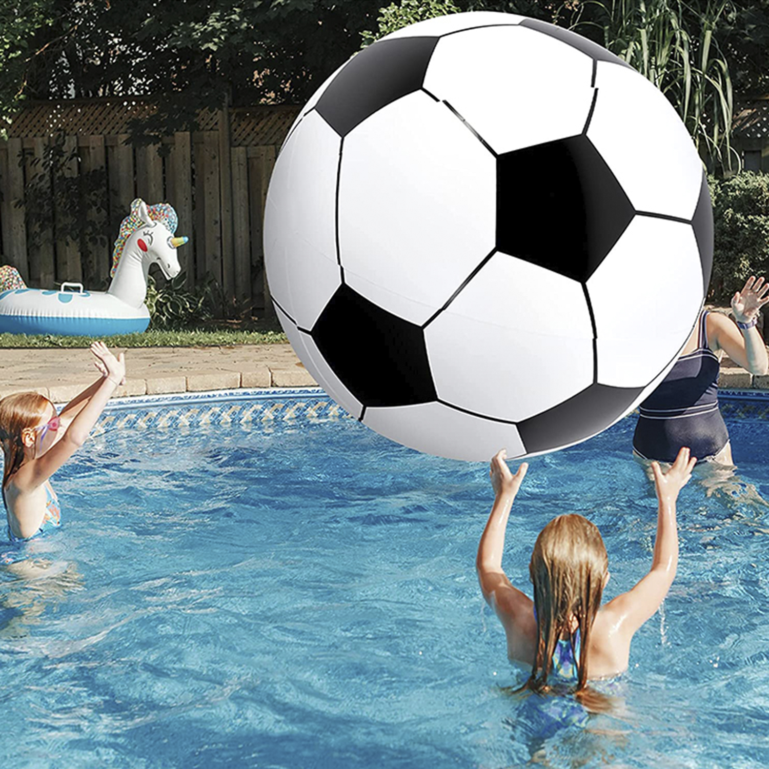 Niños juegan con balón de fútbol gigante en piscina, flotador de unicornio al fondo.