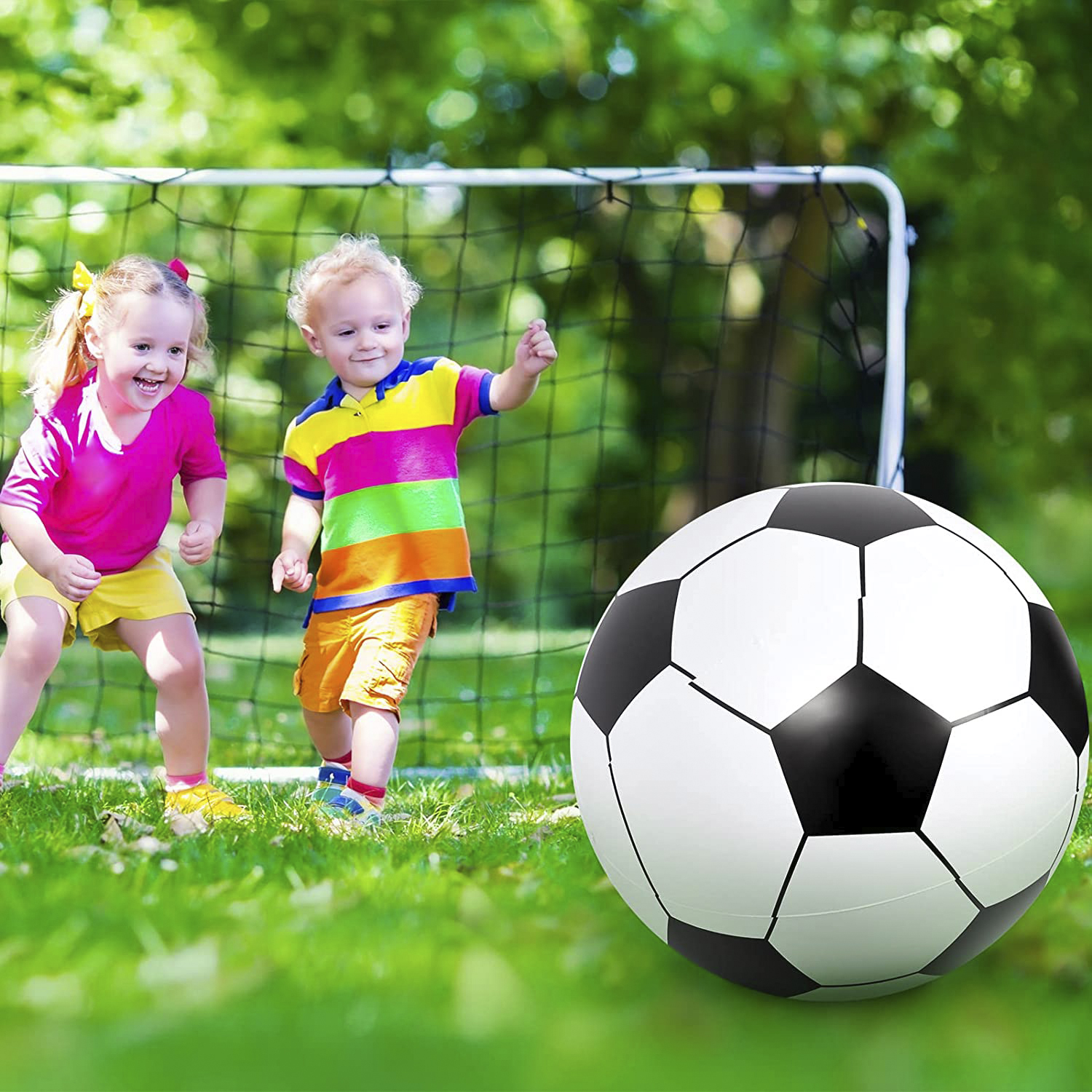 Dos niños juegan al fútbol frente a una portería, un balón de fútbol grande en primer plano.