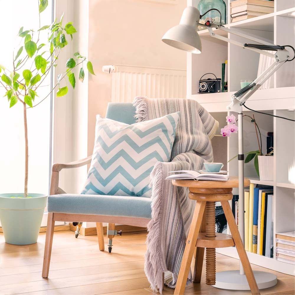 Un sillón con cojines y manta cerca de una estantería y una planta.