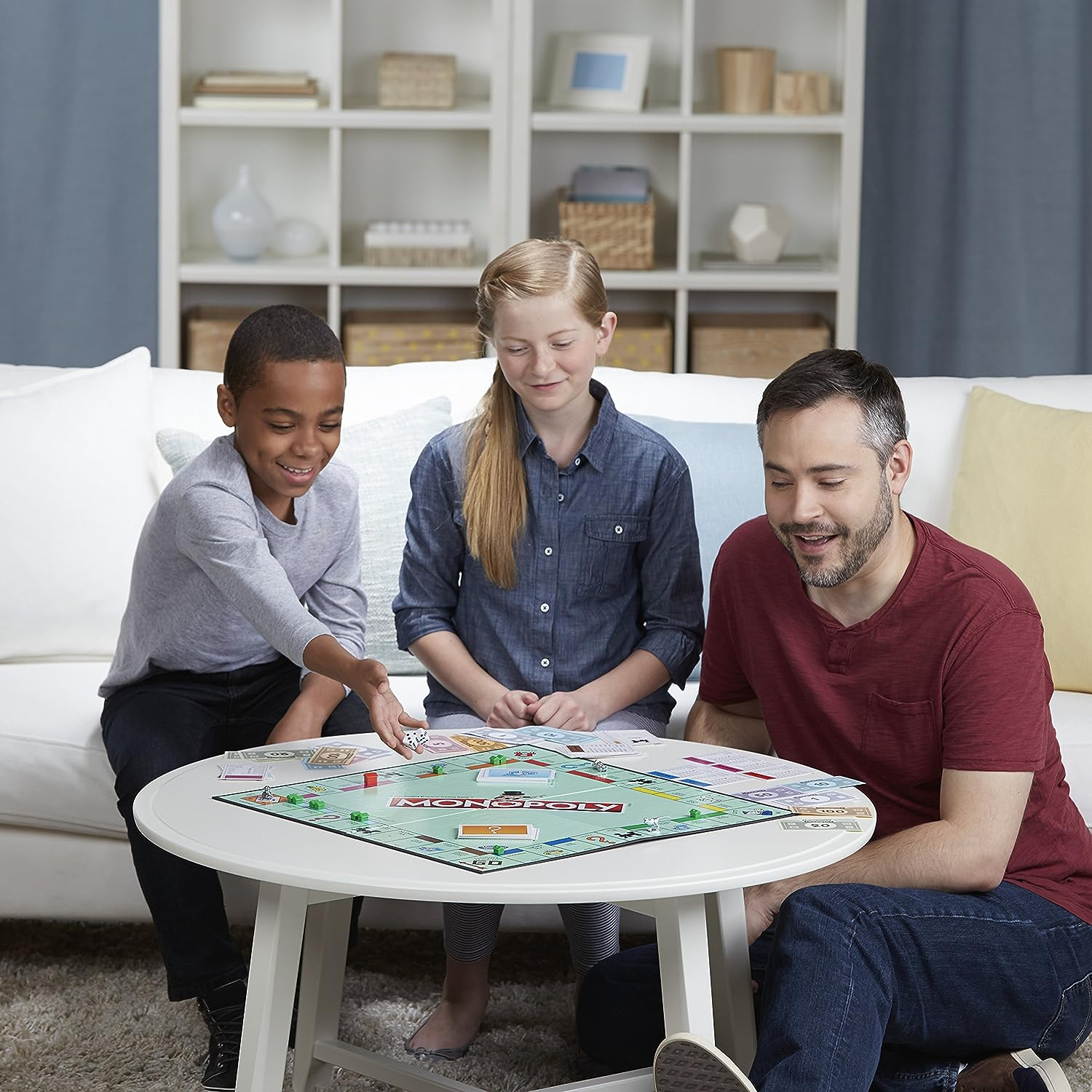 Eine Familie spielt Monopoly an einem runden Tisch im Wohnzimmer.
