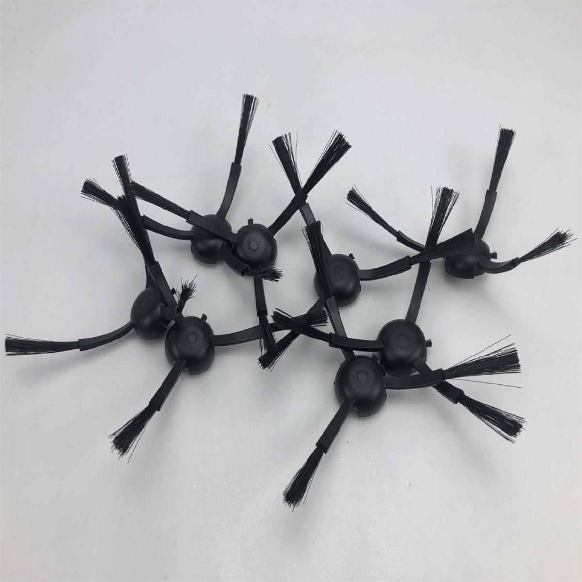 Mehrere schwarze Bürstenköpfe für einen Staubsaugerroboter liegen auf weißem Hintergrund.