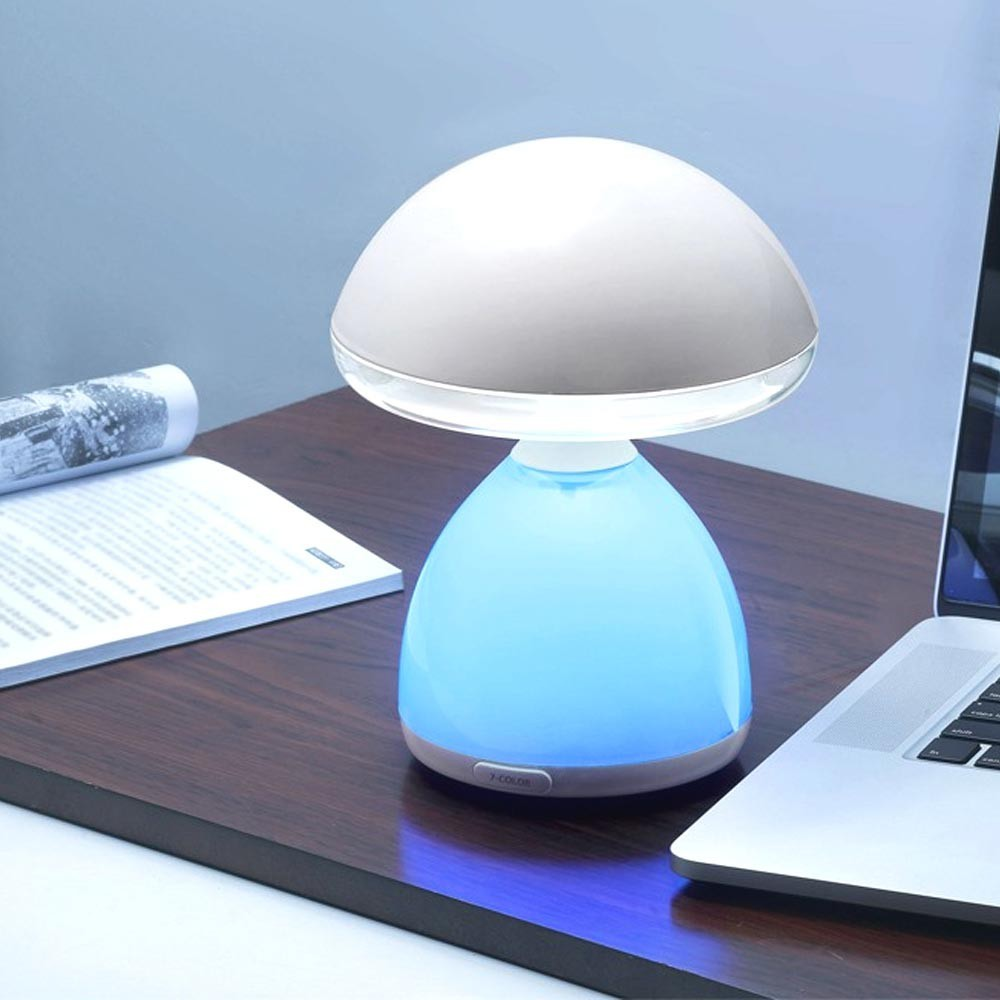 Una lámpara de hongo con luz azul está sobre un escritorio junto a una laptop y un libro.