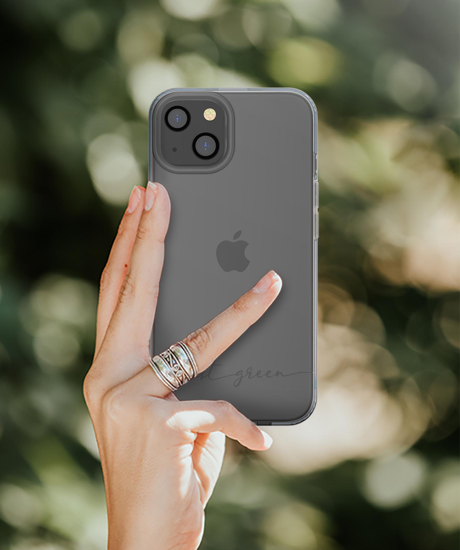 Eine Hand hält ein dunkles iPhone mit klarem Gehäuse vor unscharfem Grün.