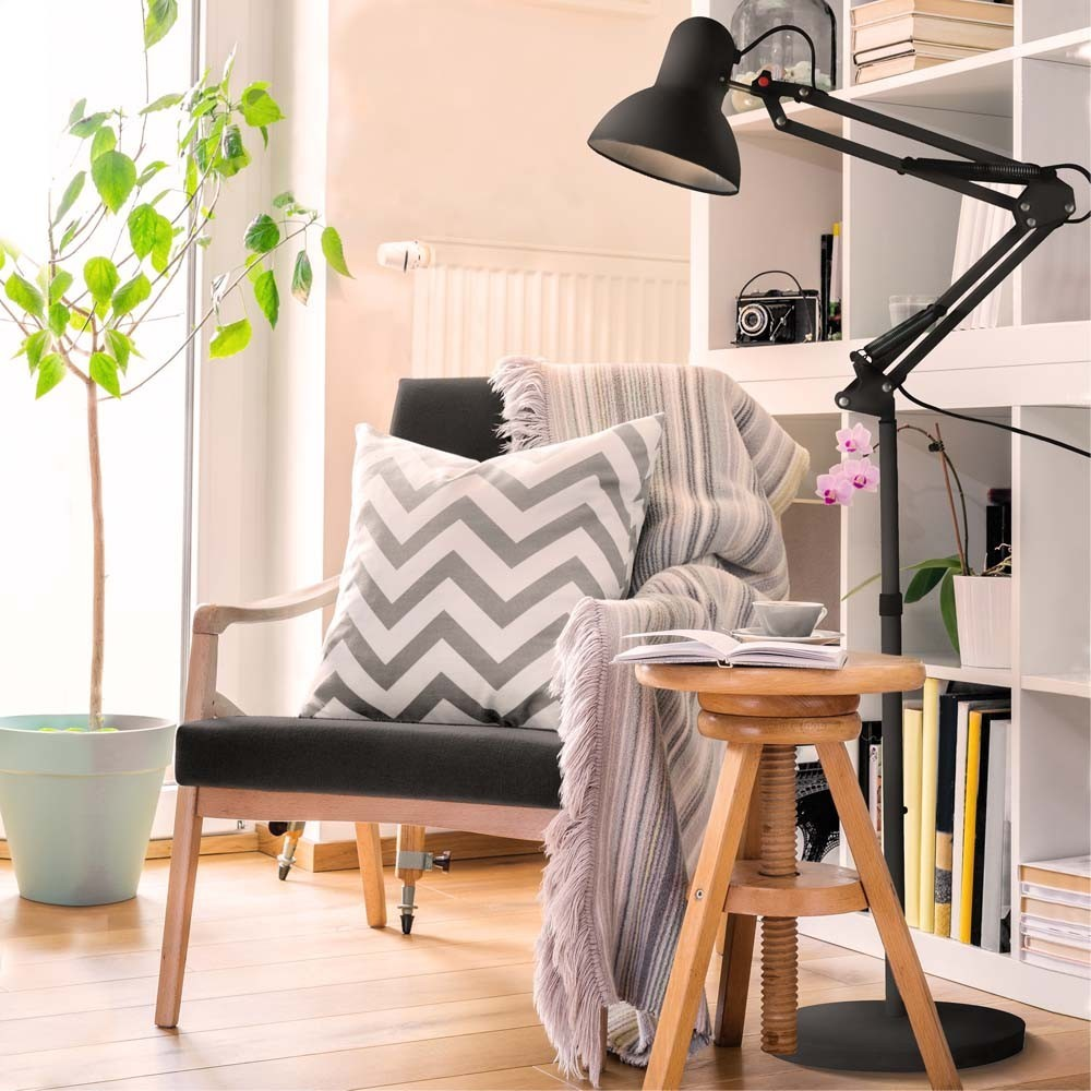Sillón con cojín y manta, junto a una mesa pequeña de madera con libro y taza.