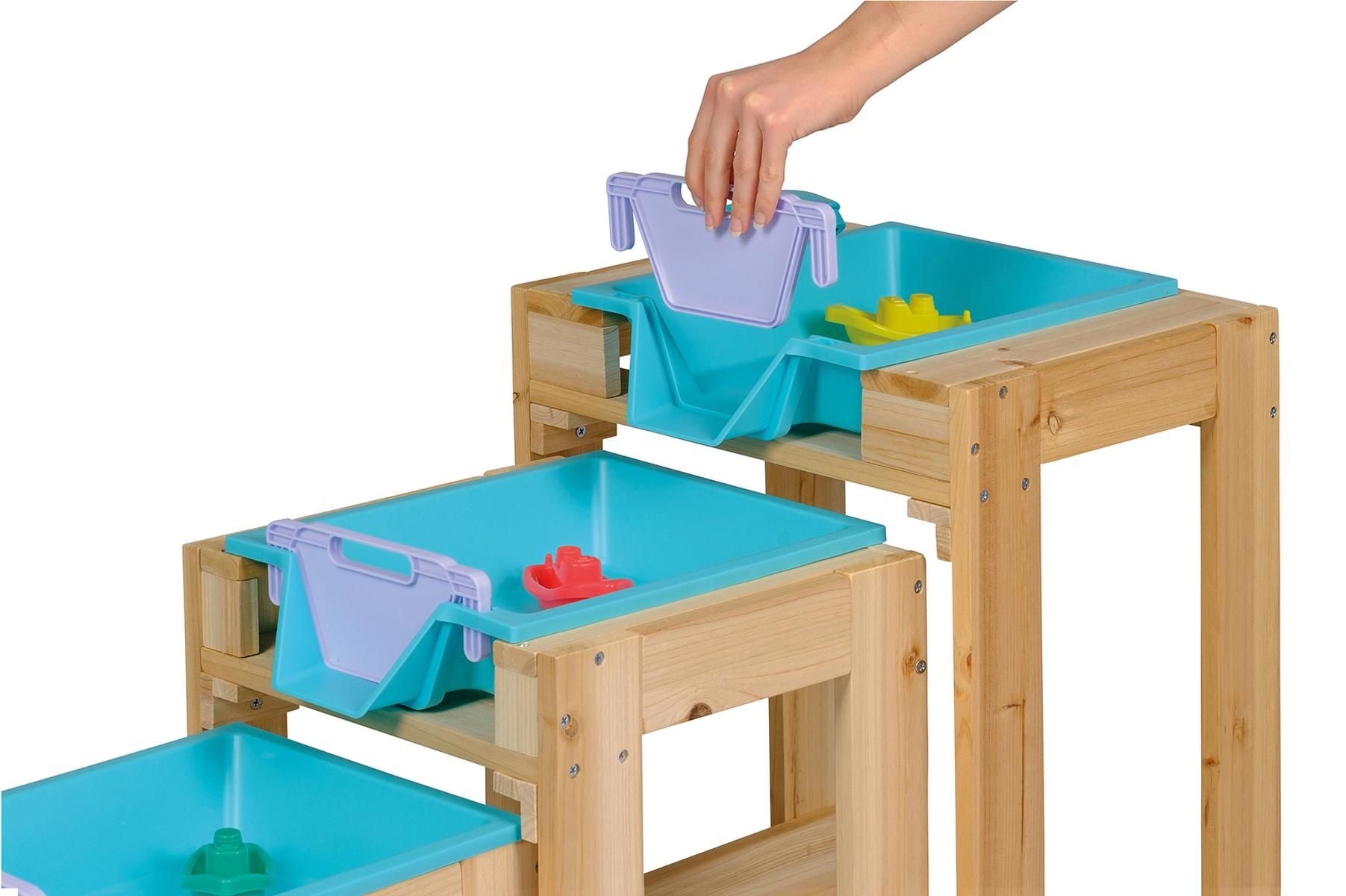 Eine Hand setzt einen lila Eimer in ein blaues Wasserbecken auf einem Holzständer.