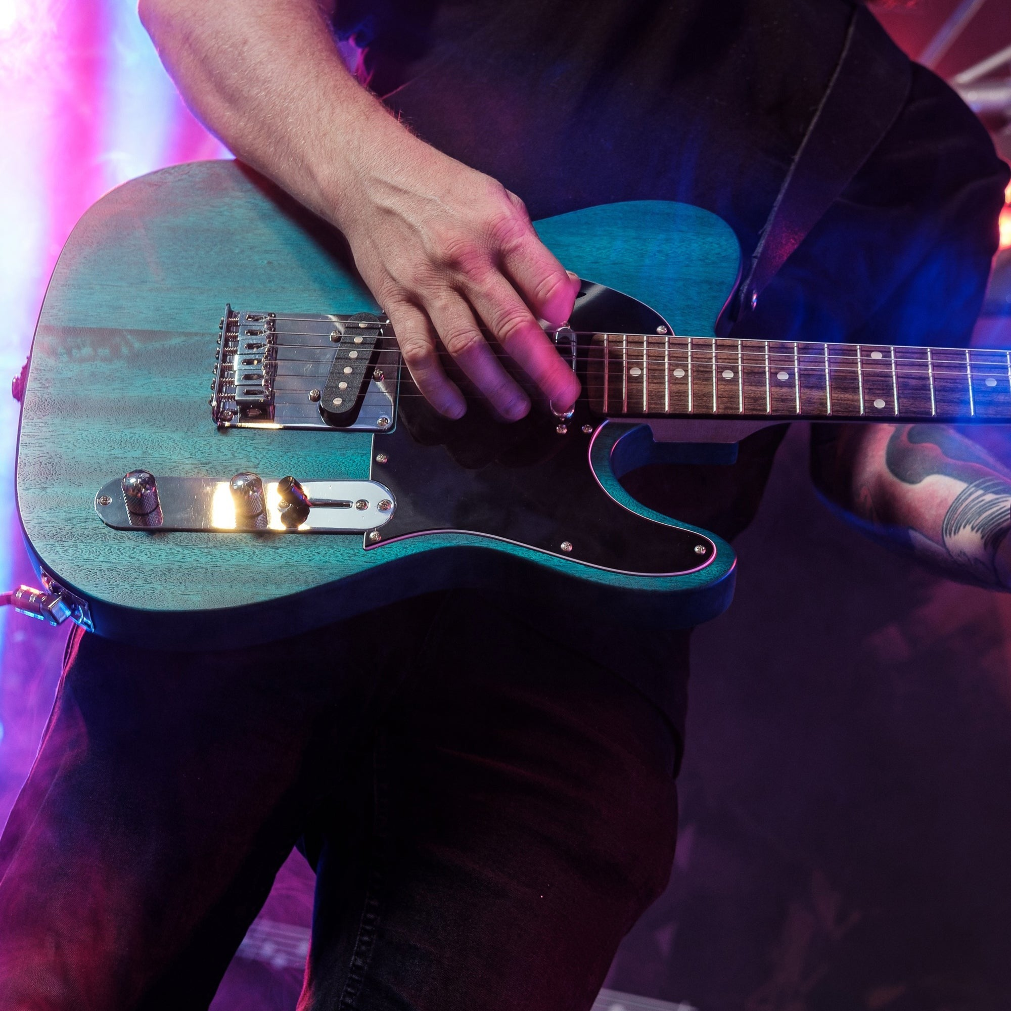 Een man bespeelt een blauwe elektrische gitaar op een concert met kleurrijke verlichting.