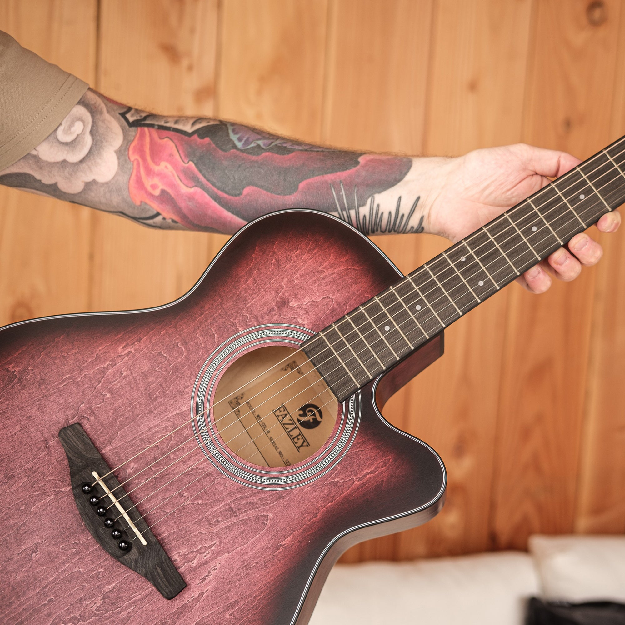 Een kastanjebruine akoestische gitaar vastgehouden door een getatoeëerde persoon.