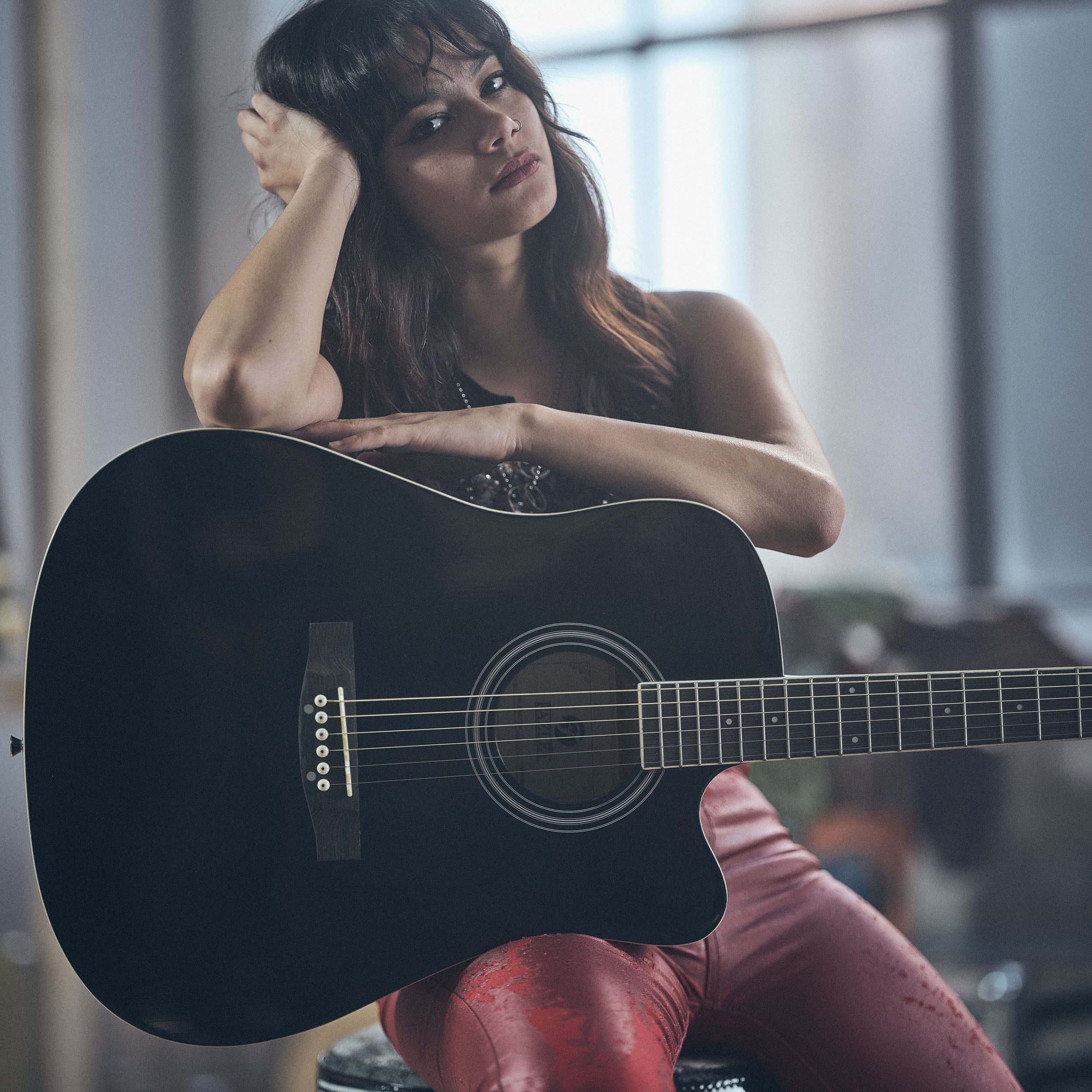 Vrouw met gitaar, rode broek, peinzende uitdrukking.