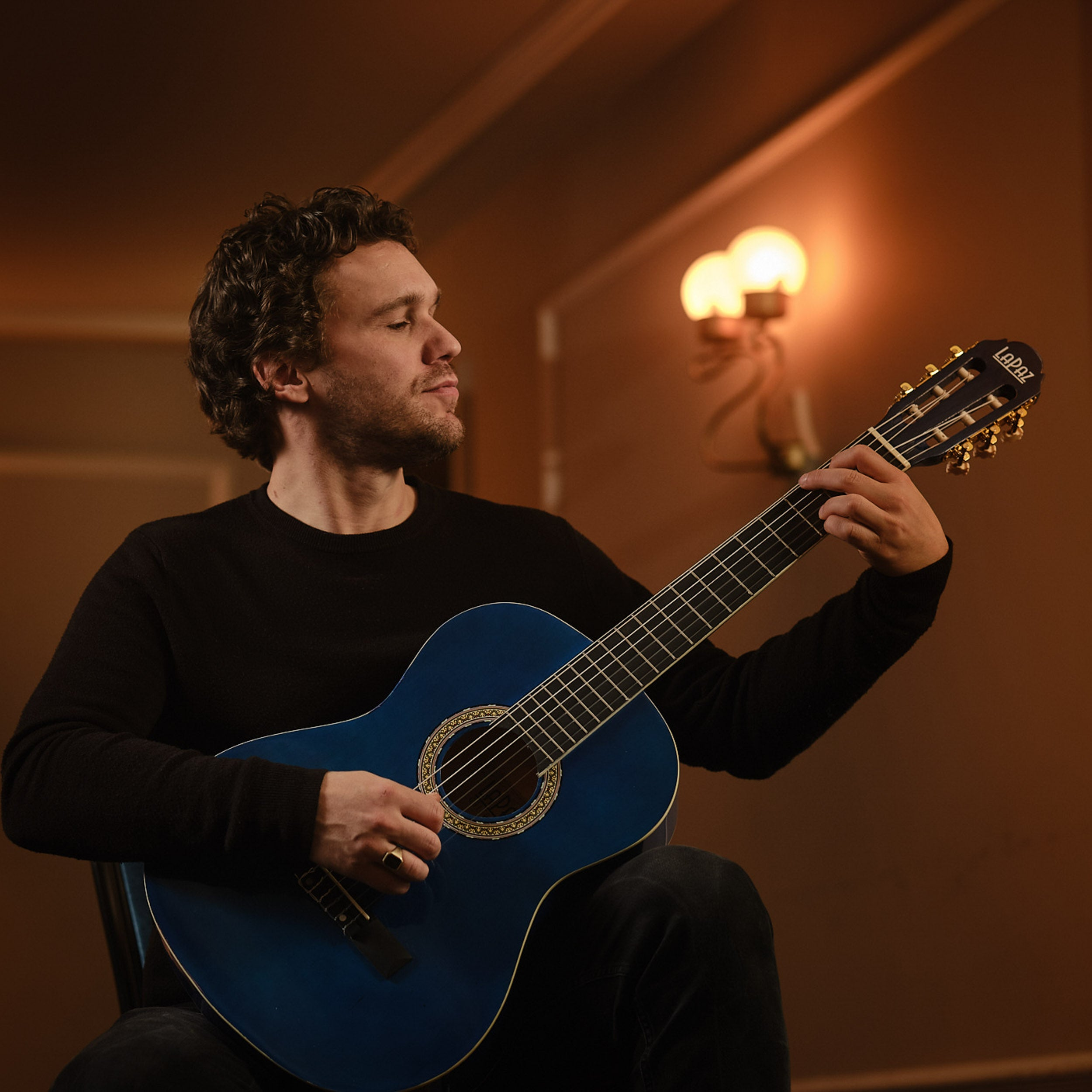 Man speelt op een blauwe gitaar in zwarte kleding in een donkere kamer.