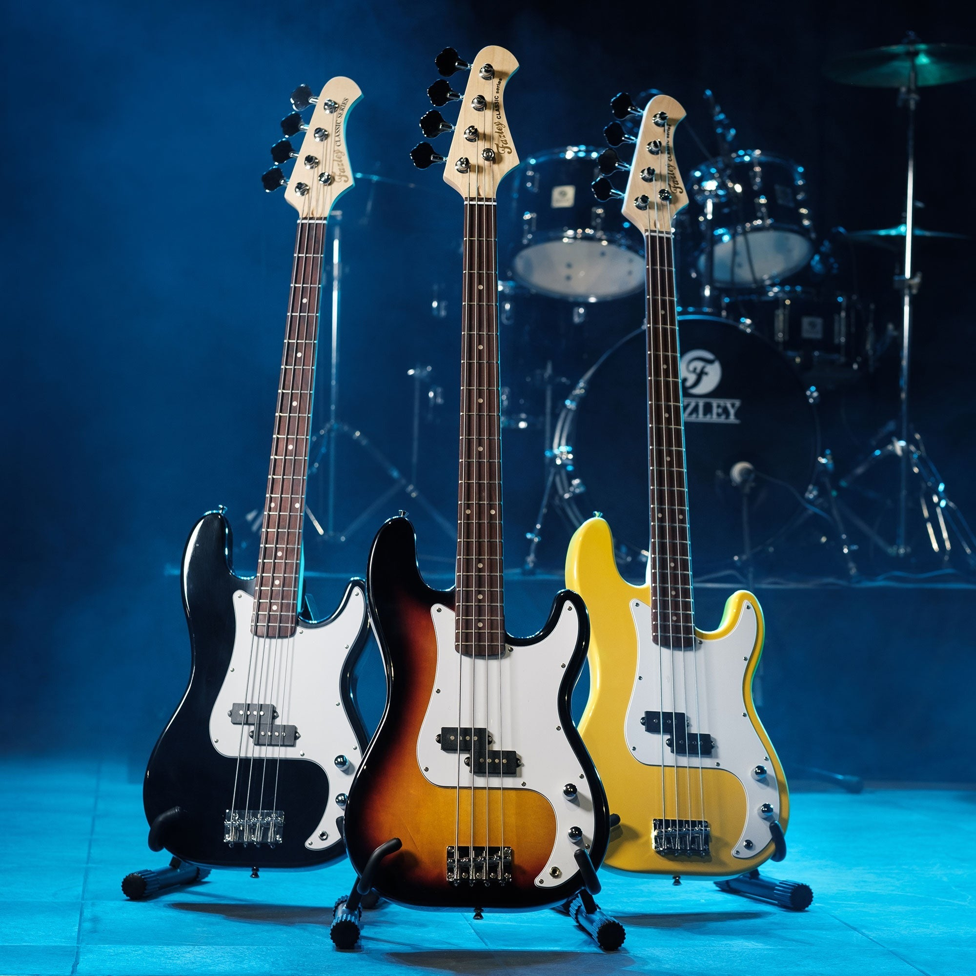 Drie elektrische basgitaren: zwart, sunburst en geel, met drumstel op achtergrond.