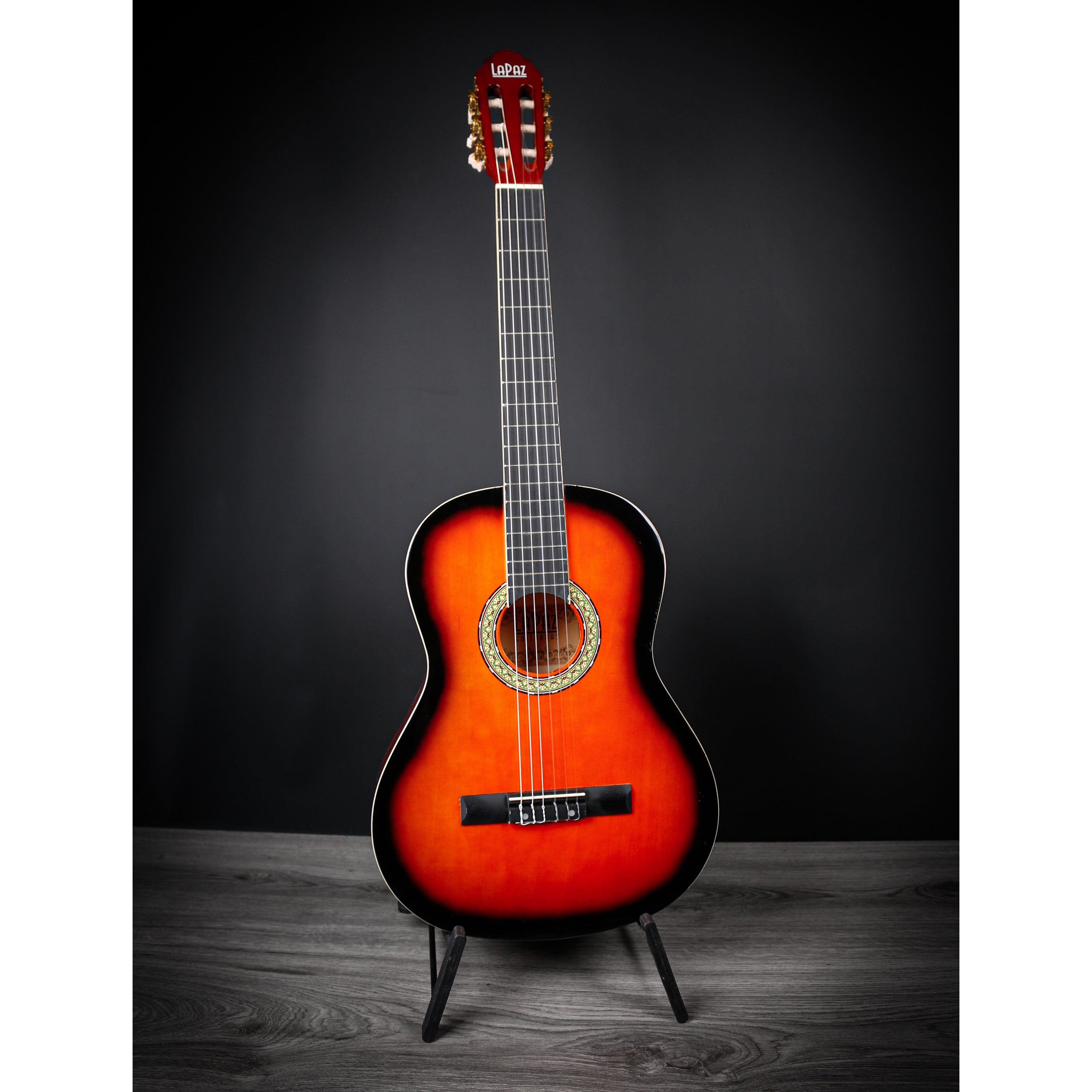 Een rood-oranje akoestische gitaar staat op een standaard tegen een donkere achtergrond.