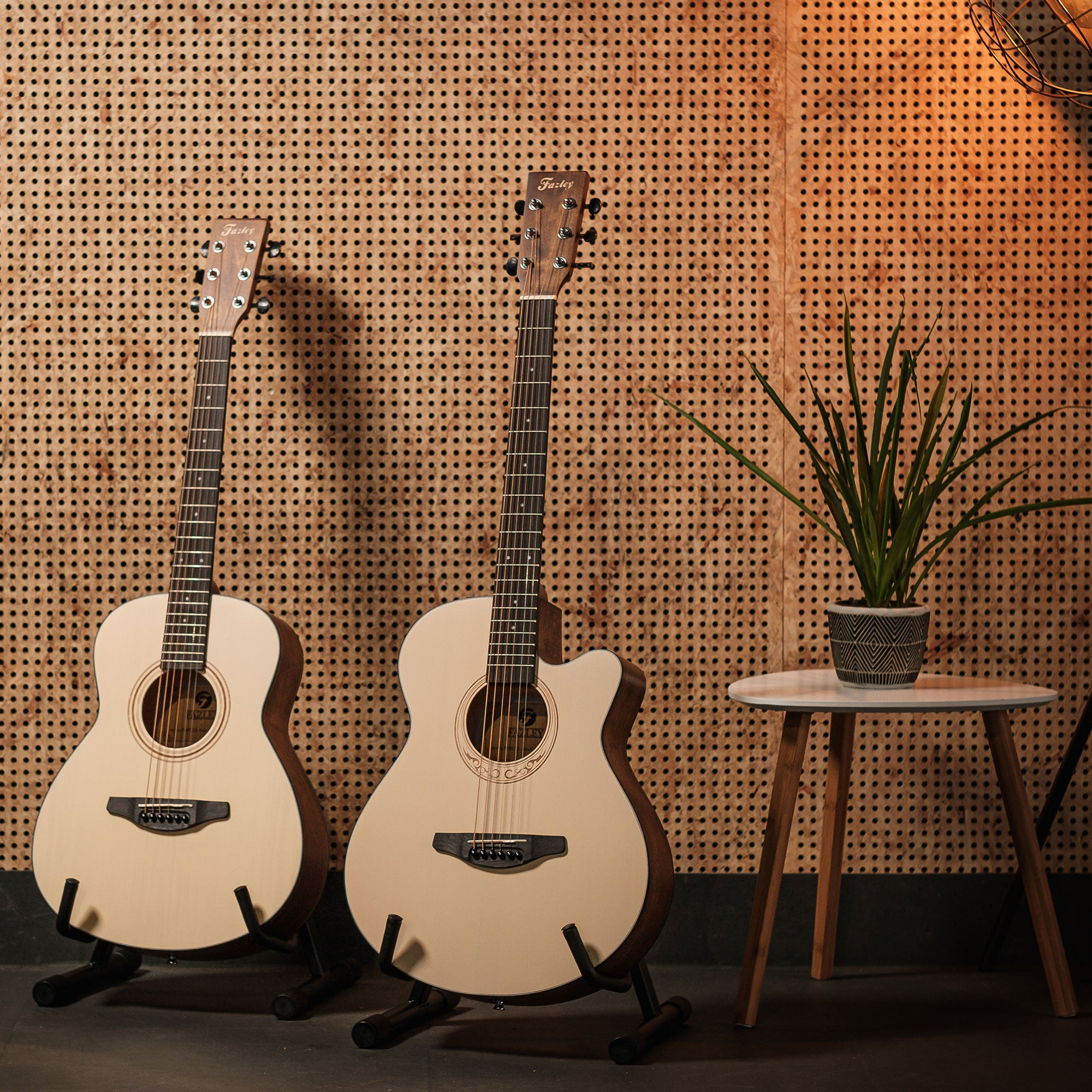 Twee lichte akoestische gitaren staan op standaards voor een houten pegboardwand.