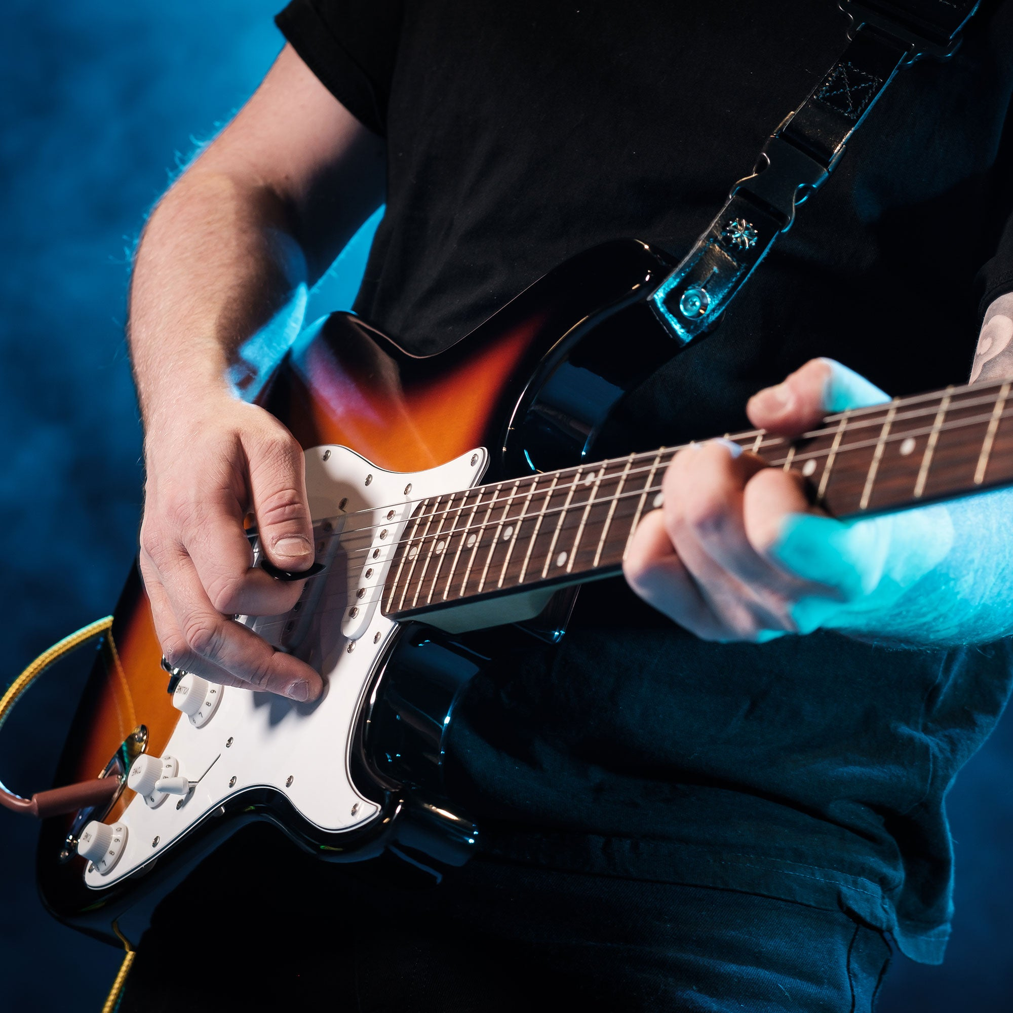 Een man bespeelt een sunburst elektrische gitaar, verlicht door blauwe rook.