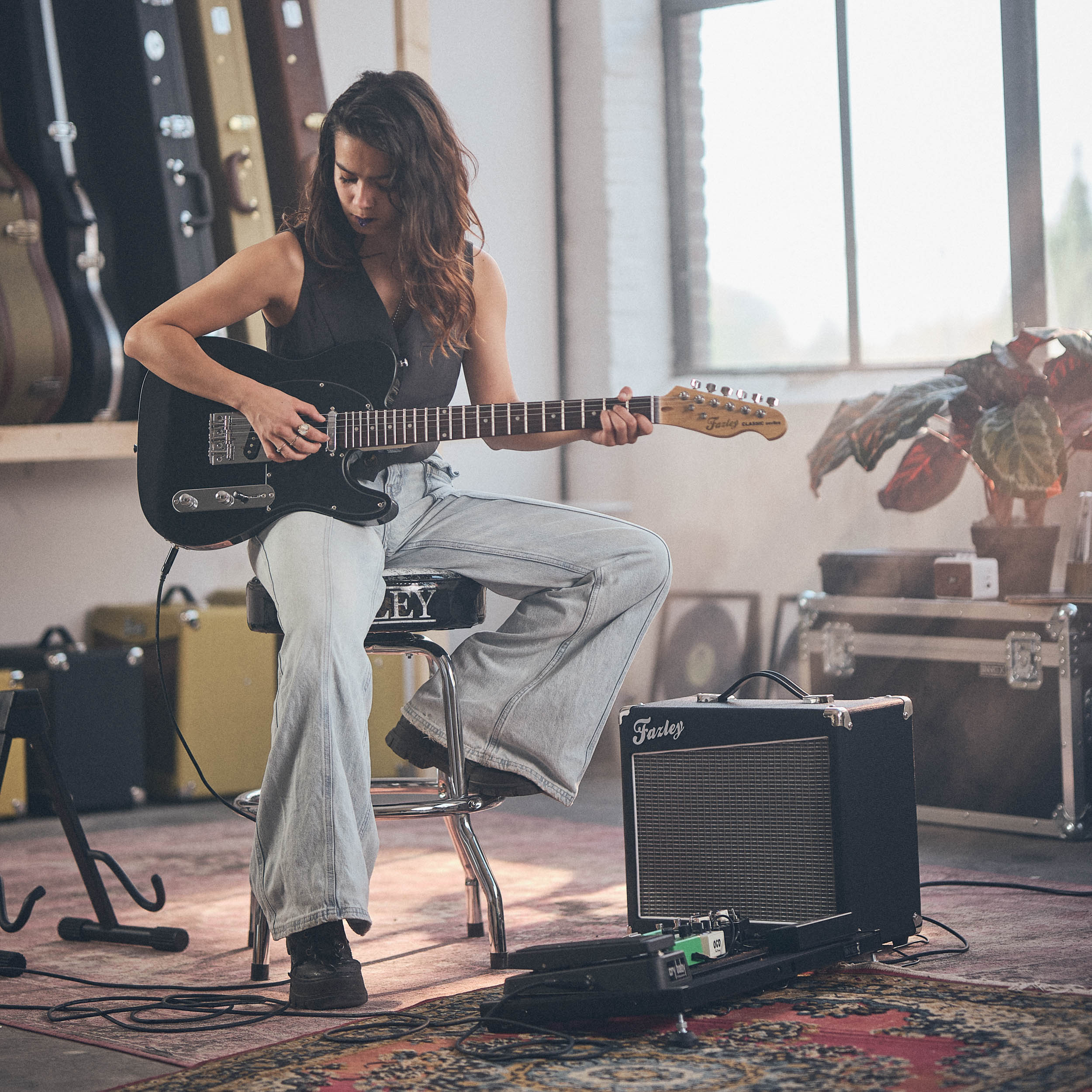 Vrouw speelt elektrische gitaar in kamer met gitaarkoffers en versterkers.
