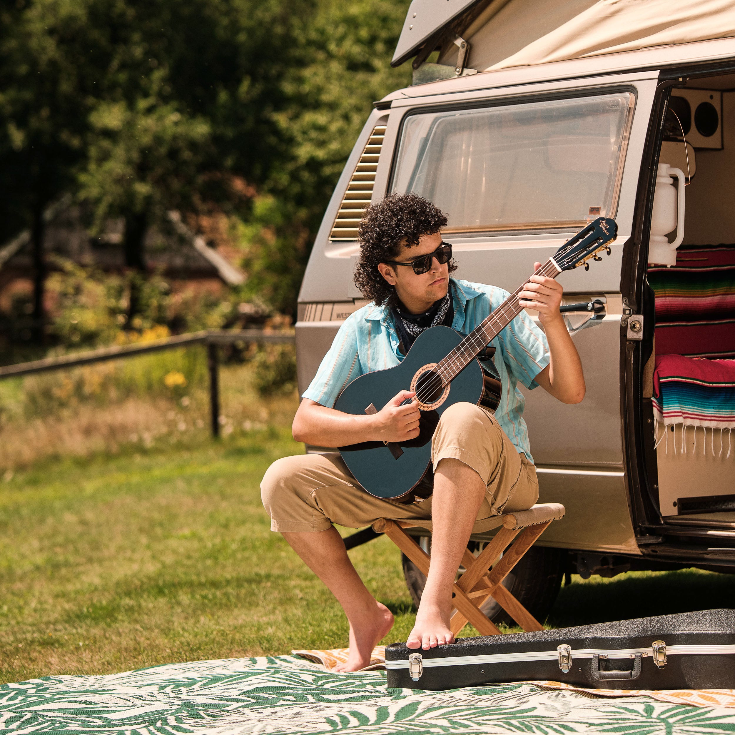 Man zit buiten gitaar te spelen naast een camper.