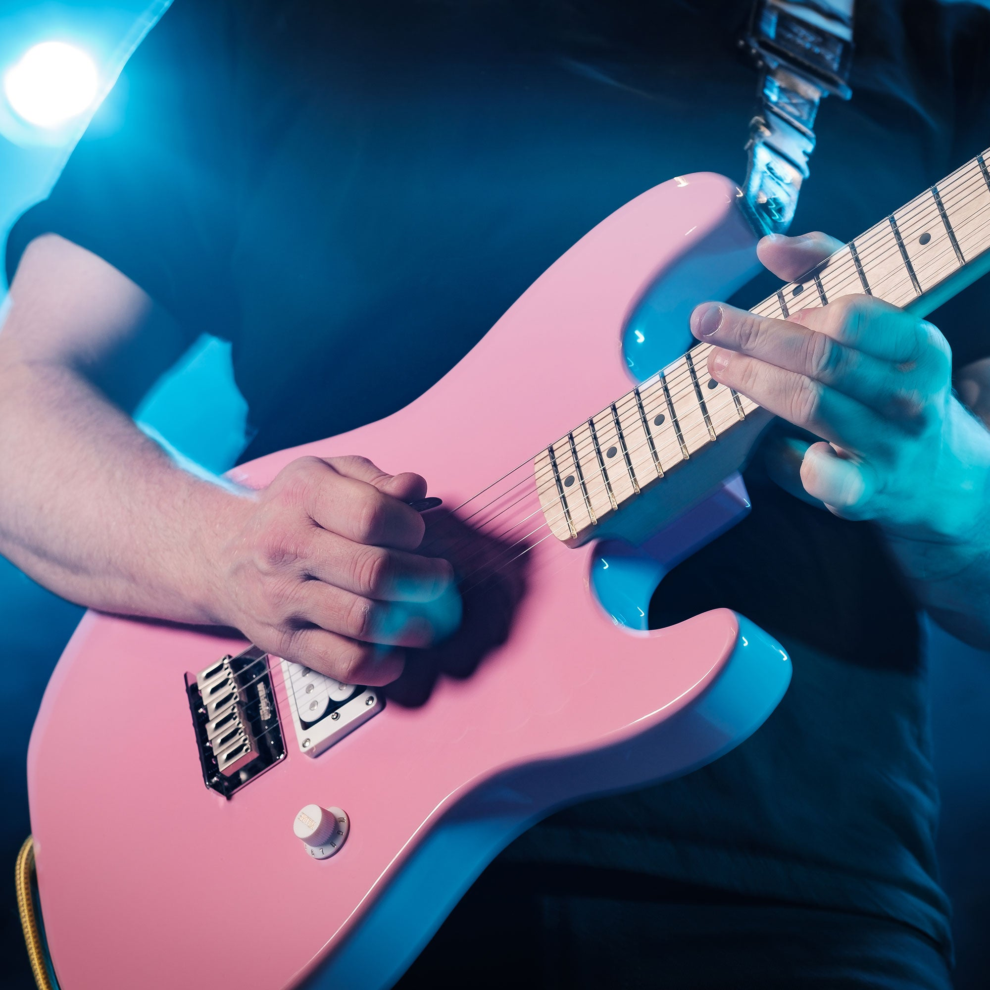 Persoon speelt een roze elektrische gitaar met blauwe verlichting.