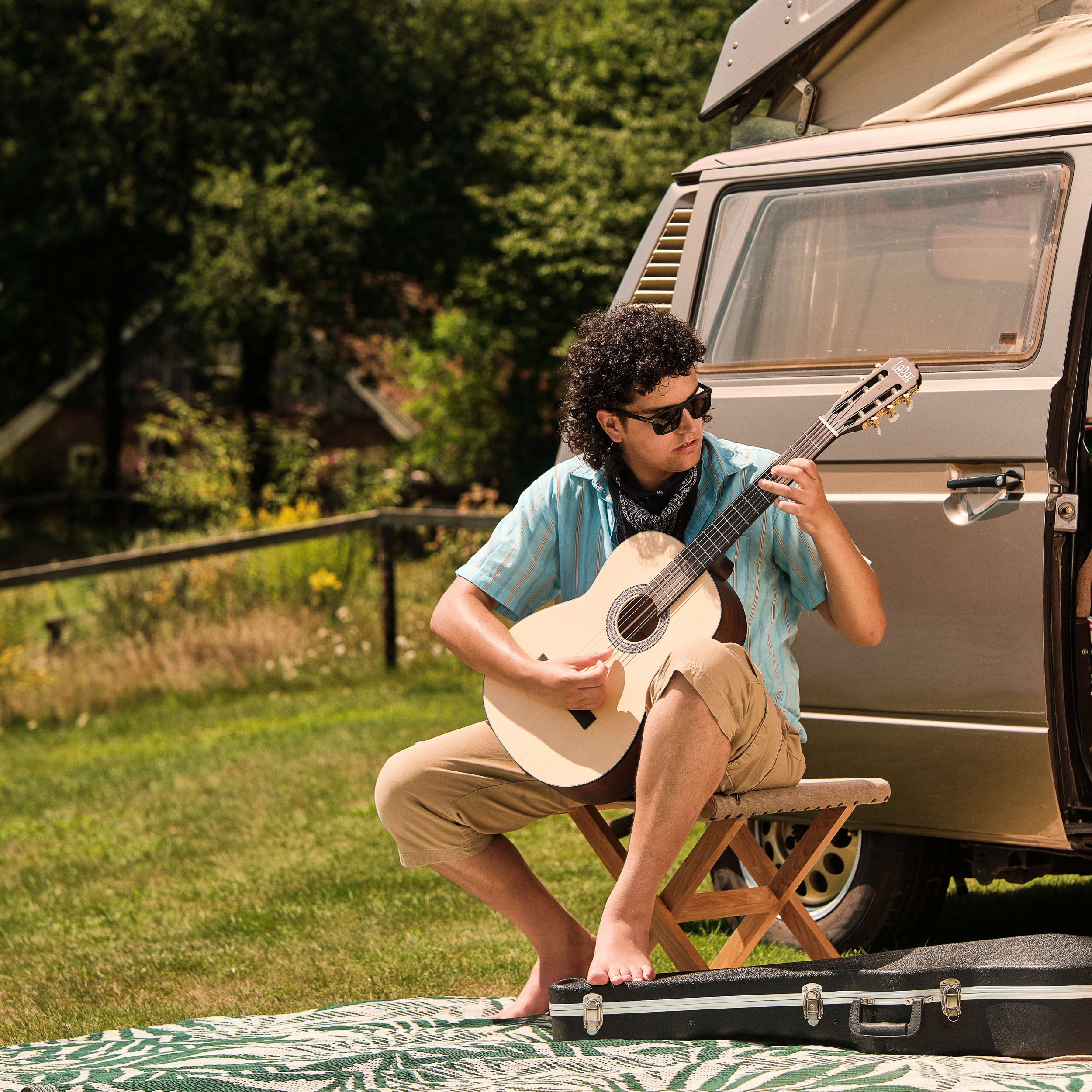 Man speelt gitaar naast een camper buiten op een deken.