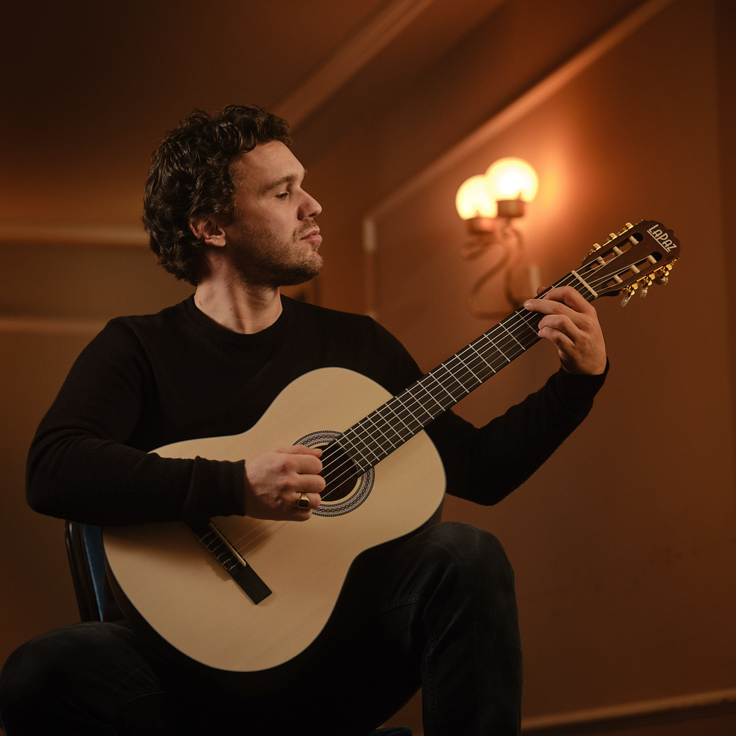 Man speelt akoestische gitaar in een donkere kamer met warm licht.