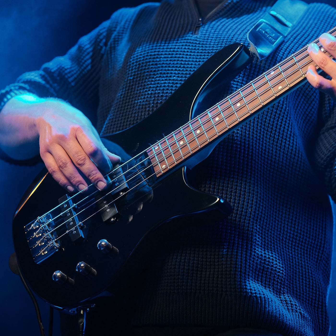 Een muzikant bespeelt een zwarte elektrische gitaar onder blauwe lichten.